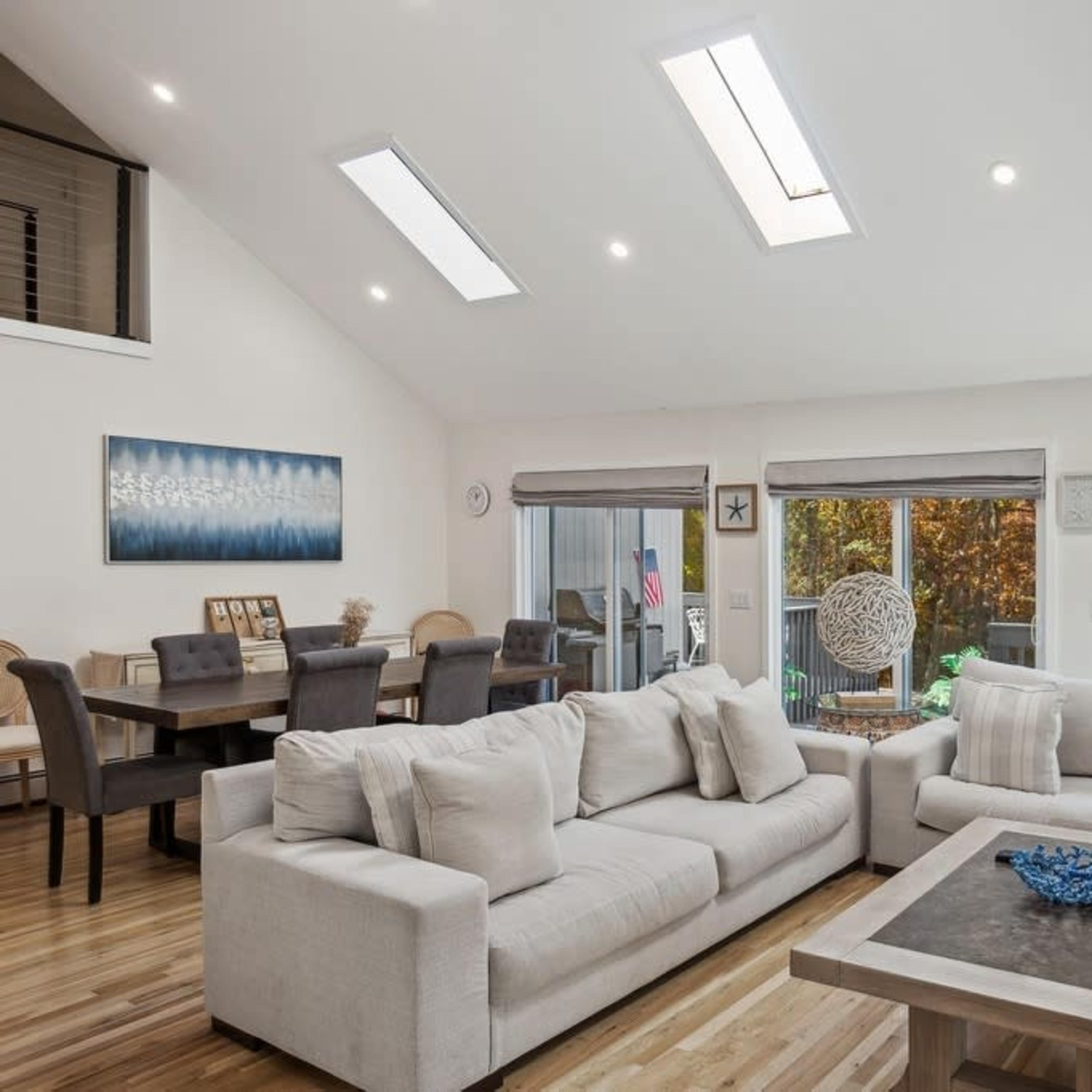 A modern living room with a light-colored sectional sofa, a coffee table, and large windows that provide ample natural light.