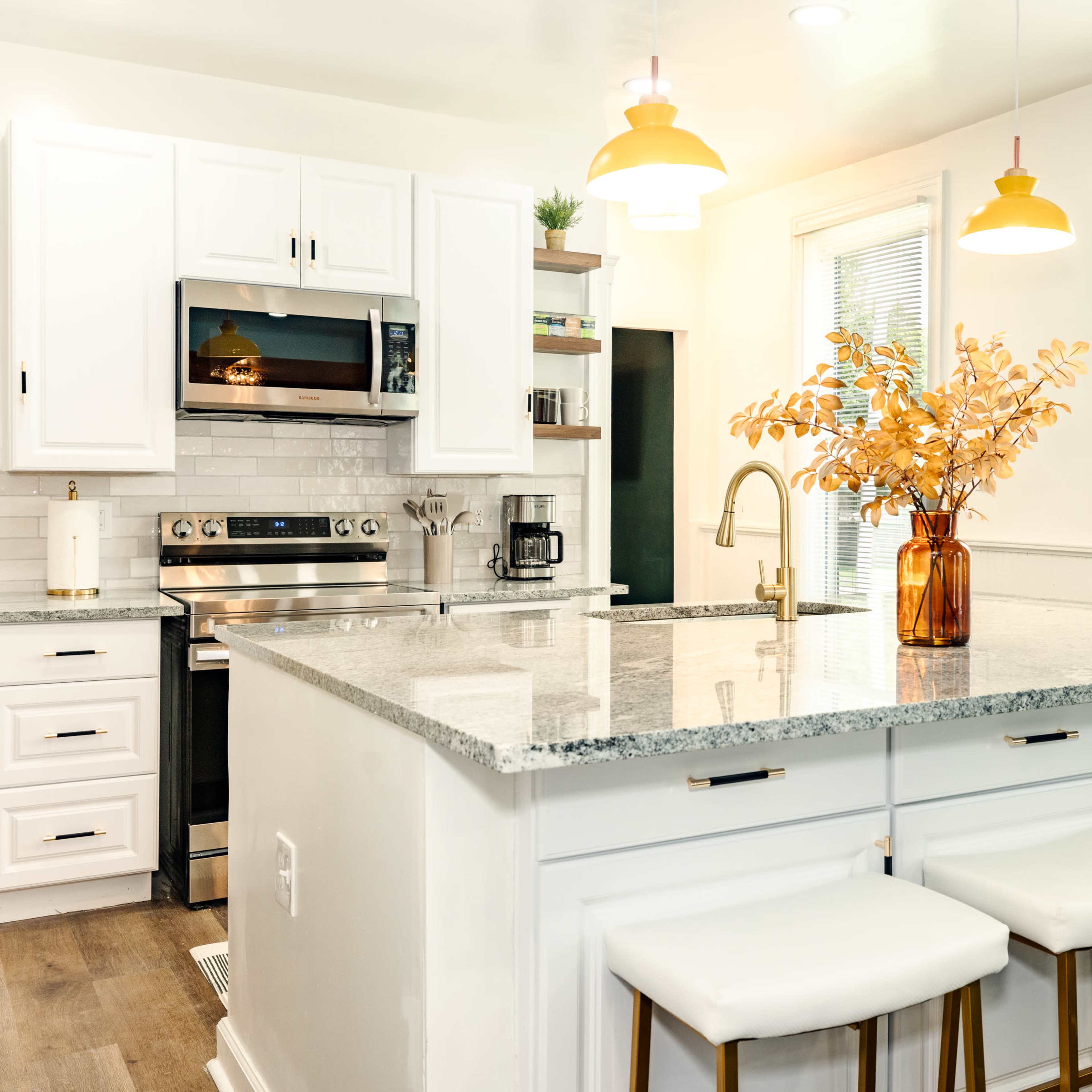 The kitchen features a central island with a granite countertop, three bar stools, and large windows that provide natural light.