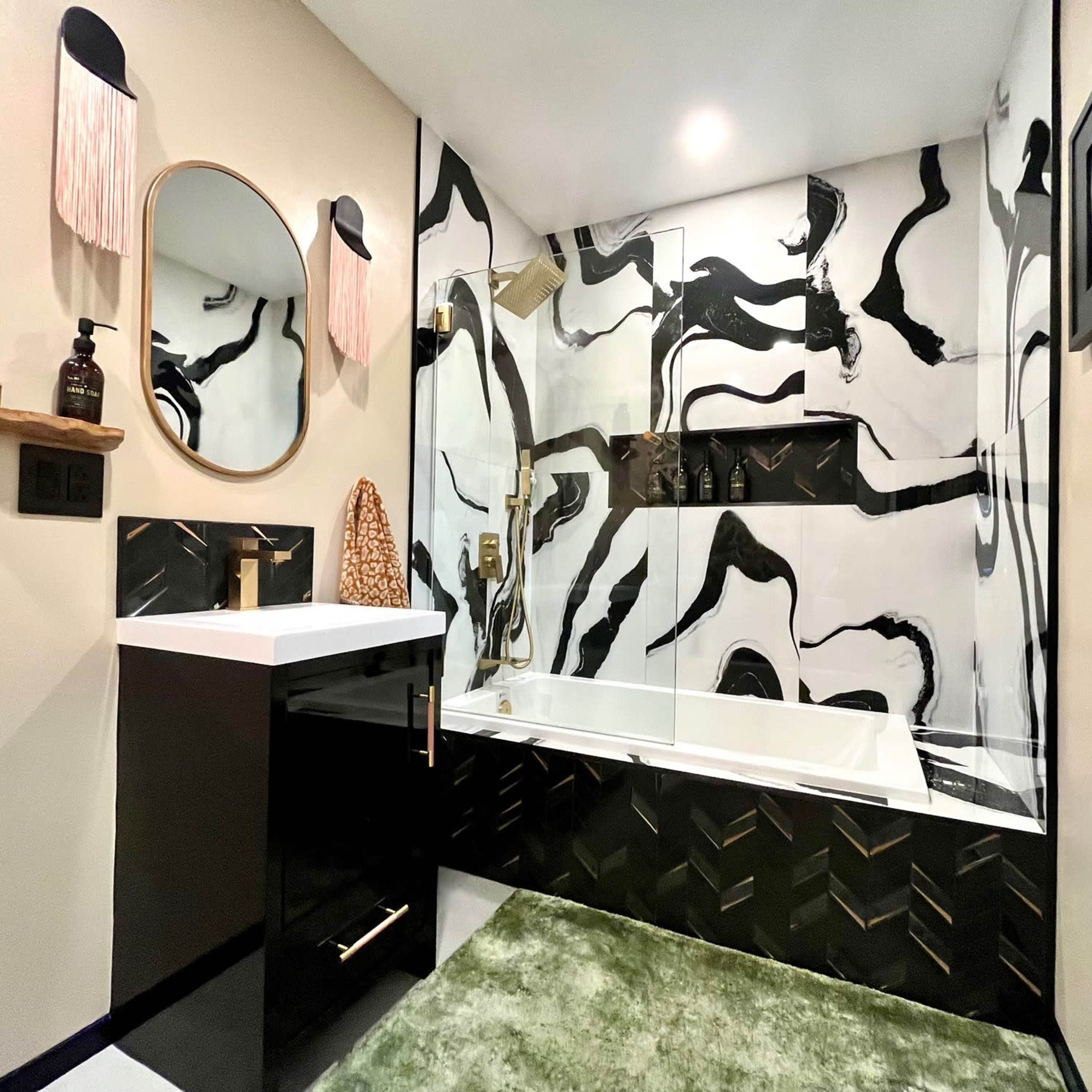 A modern bathroom featuring black and white marbled walls, a built-in shelf with decorative items, a bathtub, a sleek black vanity, and a green area rug.