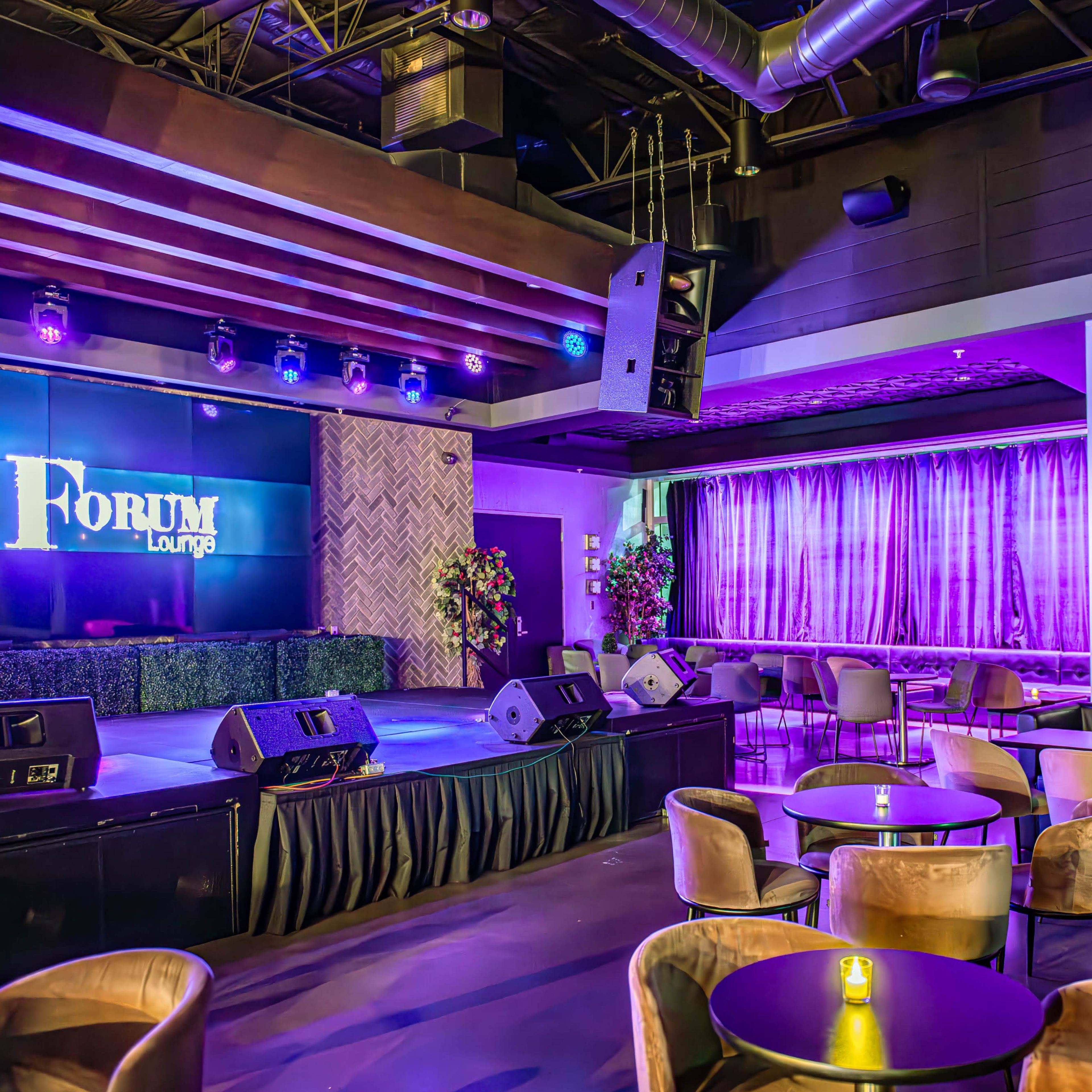 A modern lounge with a stage, seating areas, and purple lighting.