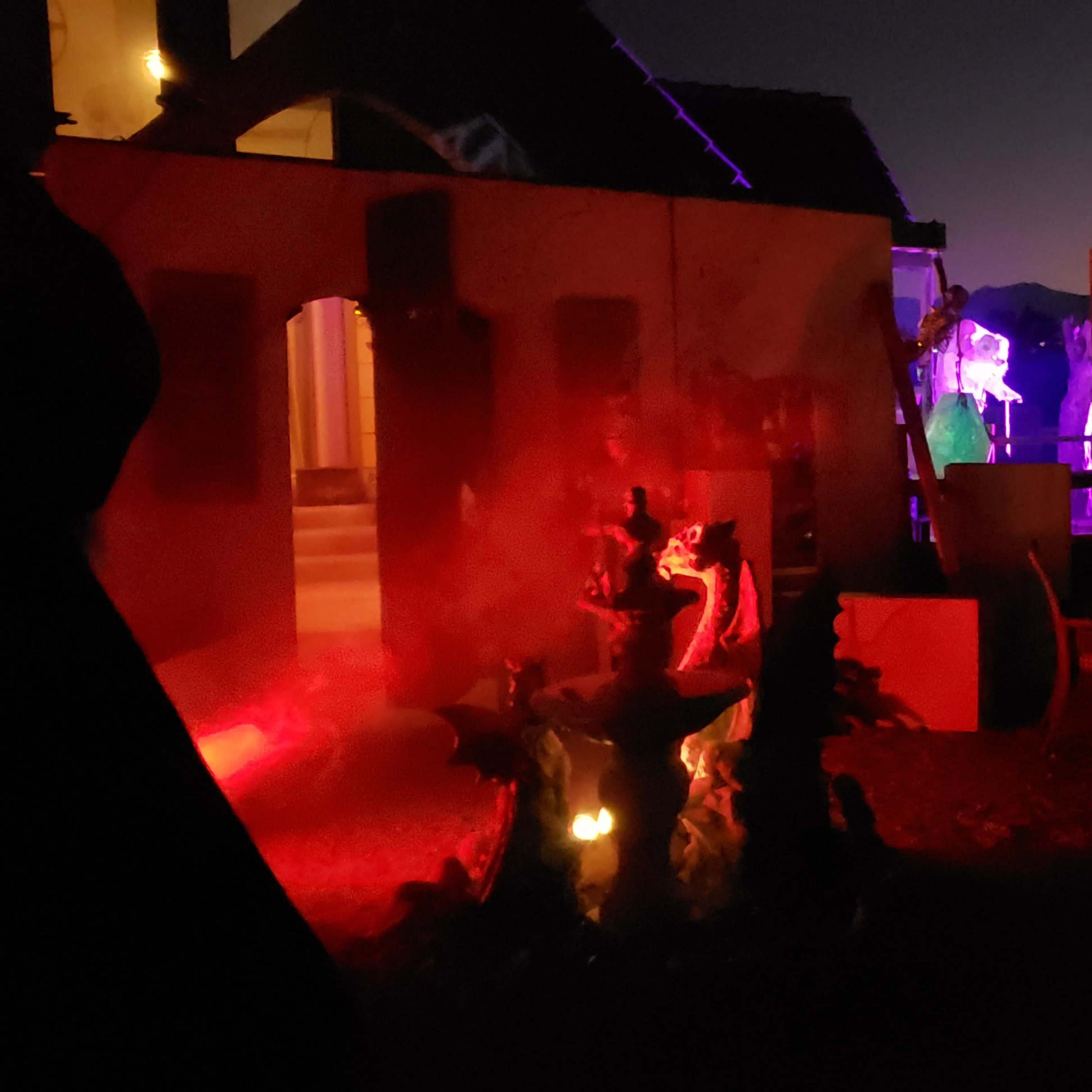 The scene shows a dimly lit outdoor area with various decorations, including a fountain, chairs, and a sign reading "Carnival," all illuminated by colorful lights against a twilight sky.