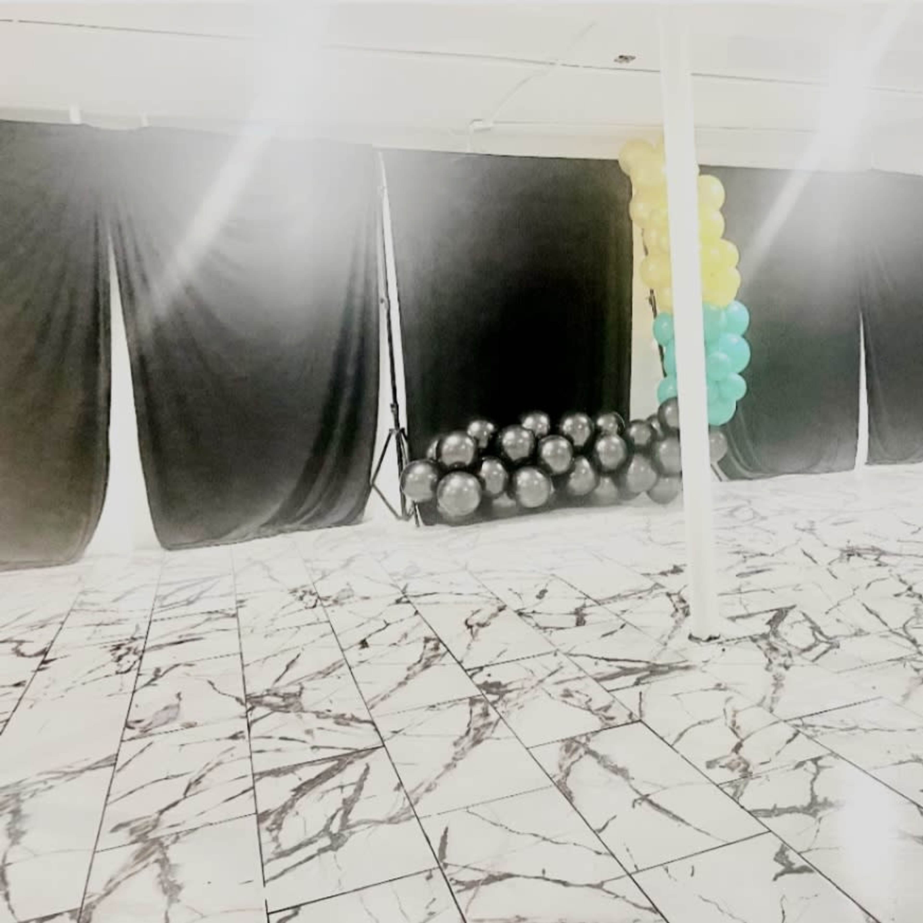 A spacious interior with a marbled floor, black drapes, and a cluster of balloons in teal and yellow on one side.