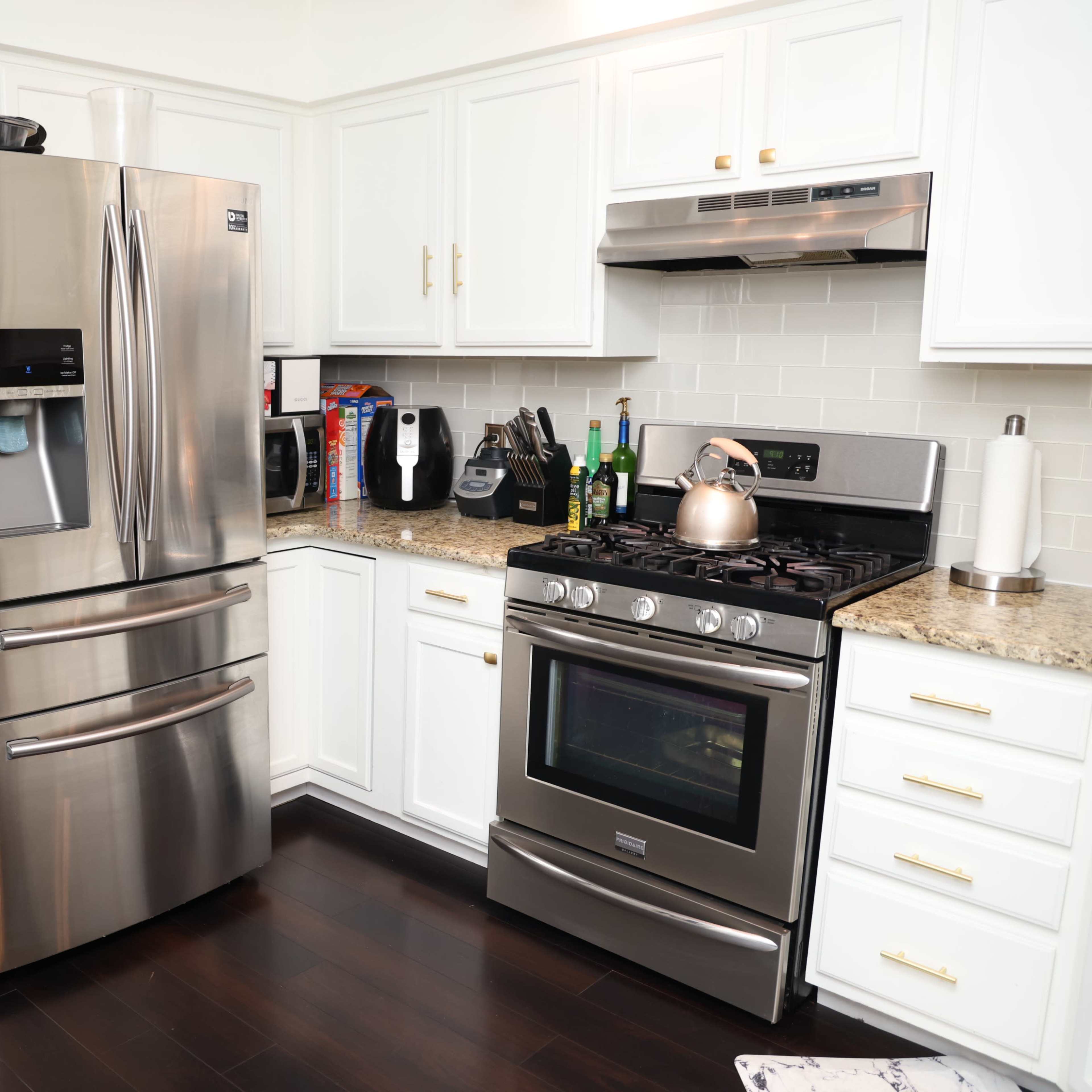 A modern kitchen with stainless steel appliances, including a refrigerator and a stove, set against white cabinetry and a granite countertop.