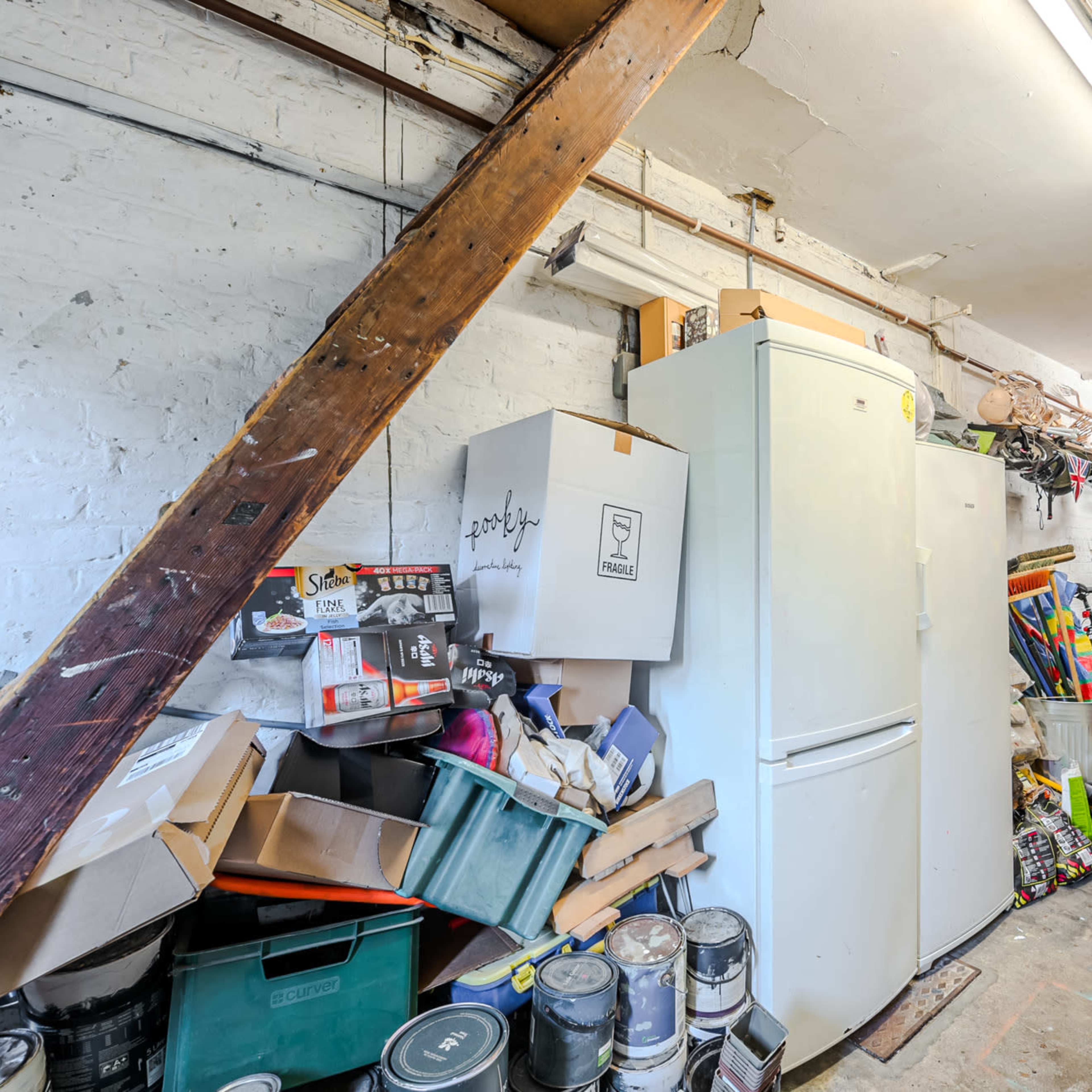 A cluttered garage with a white refrigerator, stacked boxes, and bicycles leaning against the wall.