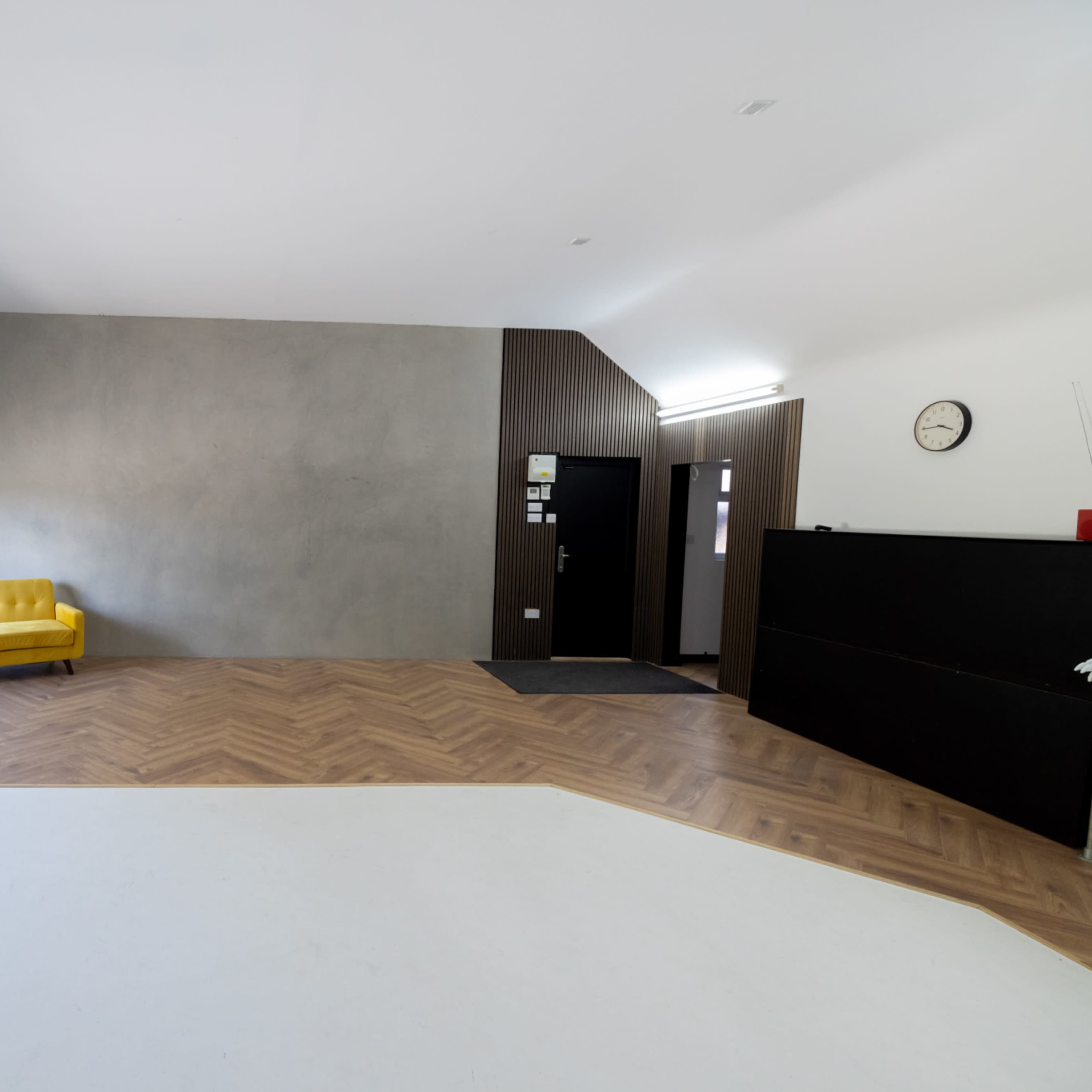 A spacious studio with a yellow sofa, large windows, and a combination of a wood and concrete wall.