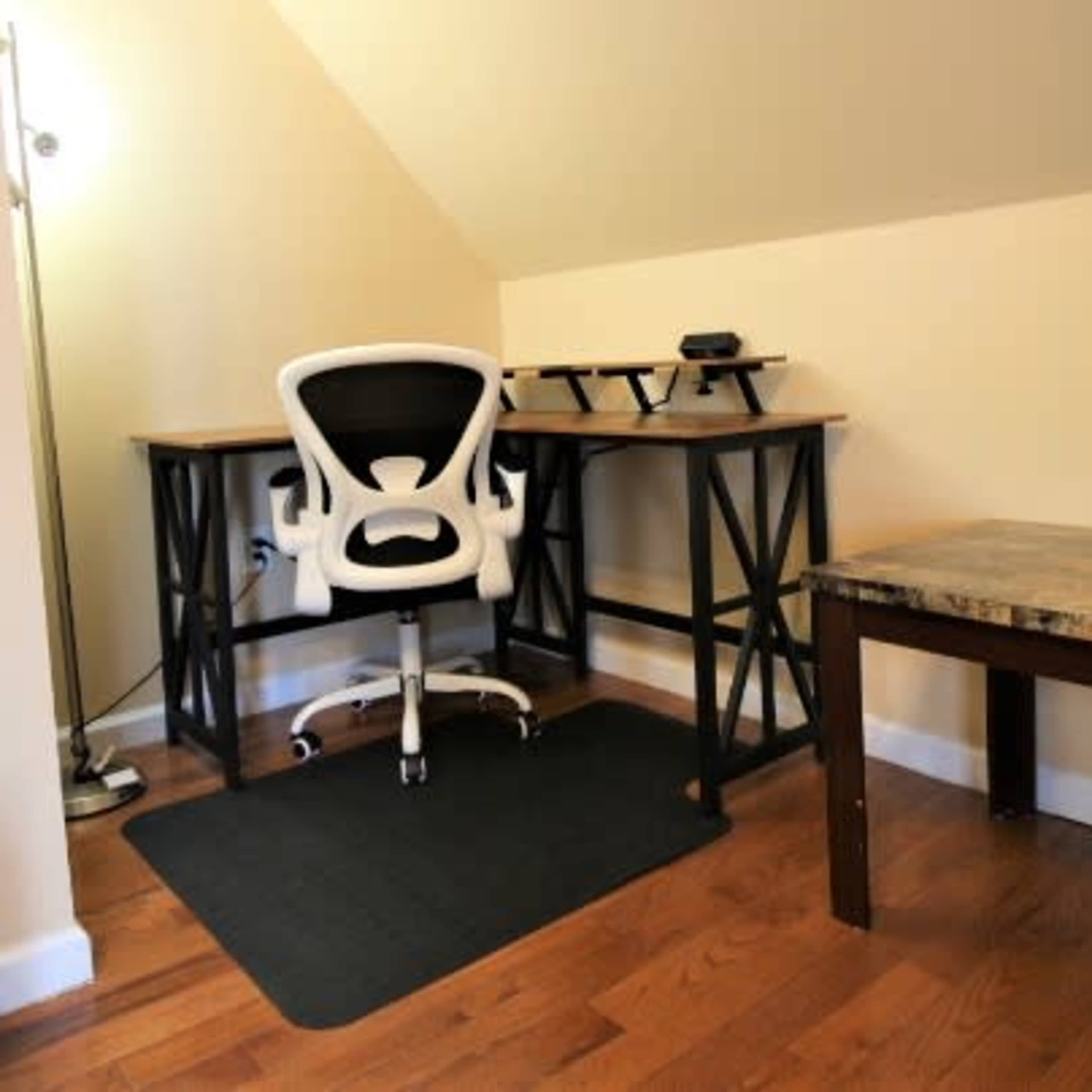 A home office setup featuring a white ergonomic chair at a wooden desk with a small shelf, accompanied by a side table and a lamp.
