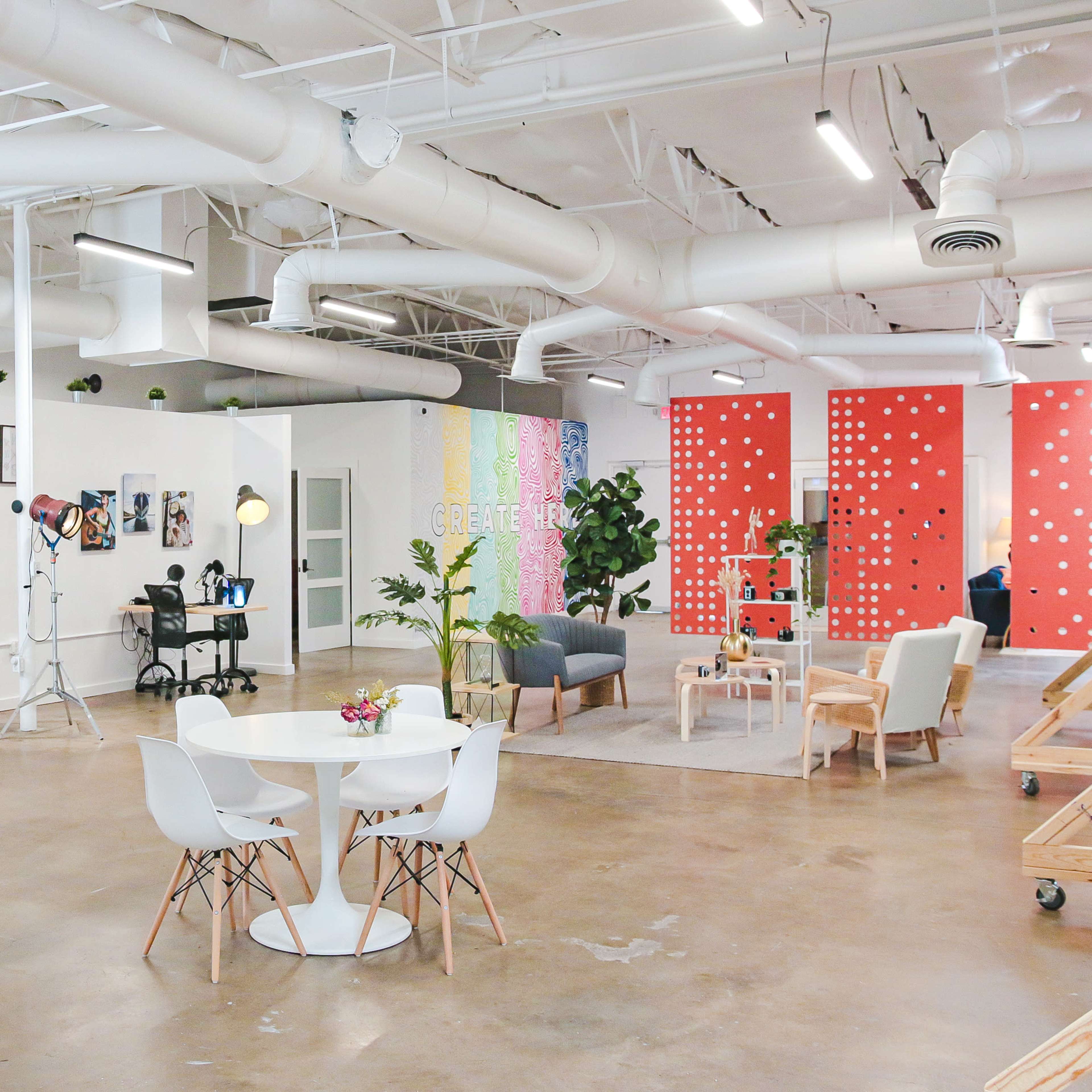A bright, open workspace featuring a seating area, a round table with chairs, various artworks on the walls, and several workstations with computers.