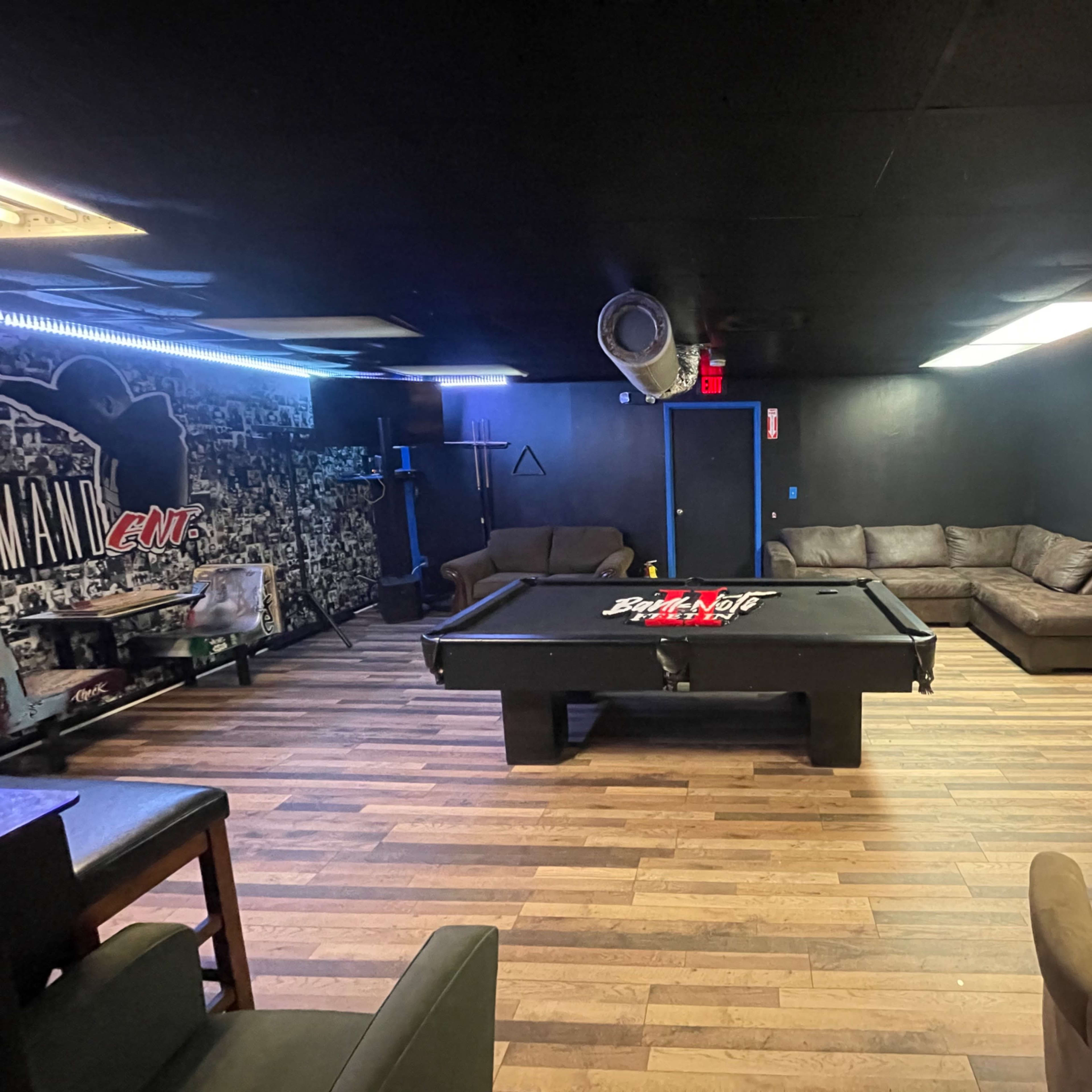 A dark room with a pool table in the center, surrounded by couches and a coffee table.