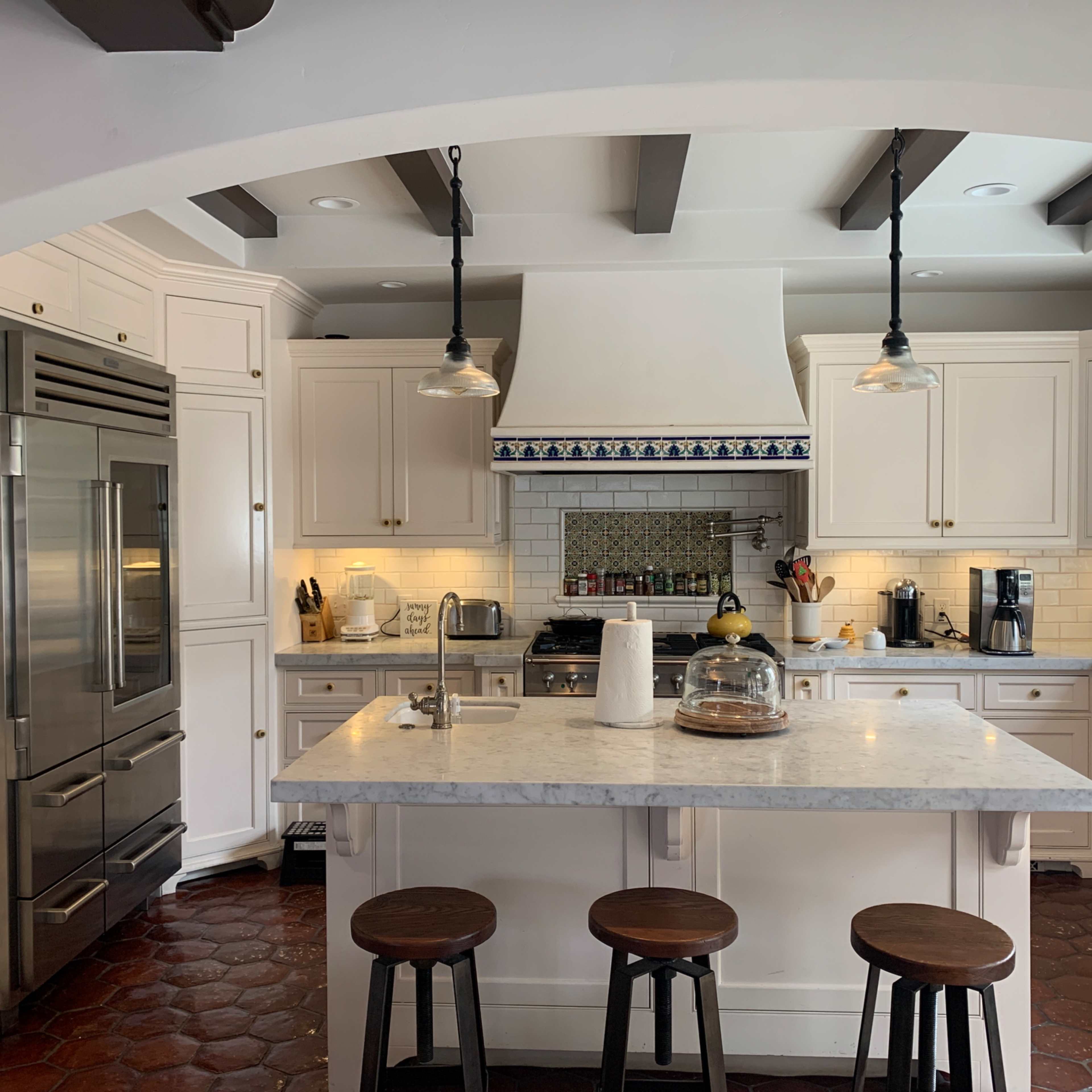 A spacious kitchen featuring white cabinets, a large marble island, and a tile backsplash with an archway leading into the room.