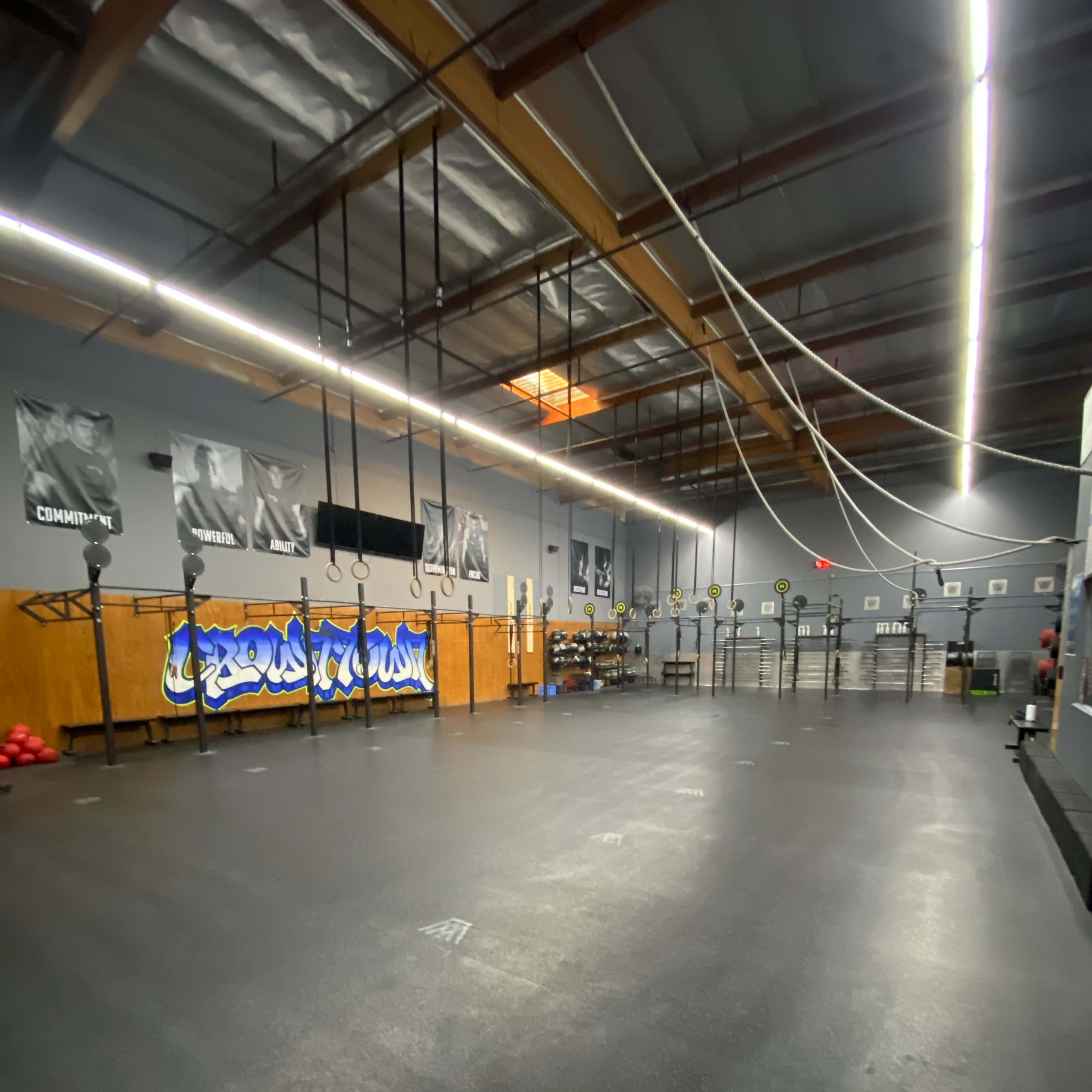 A spacious gym interior with various exercise equipment, including weights, ropes, and a wall with motivational banners.
