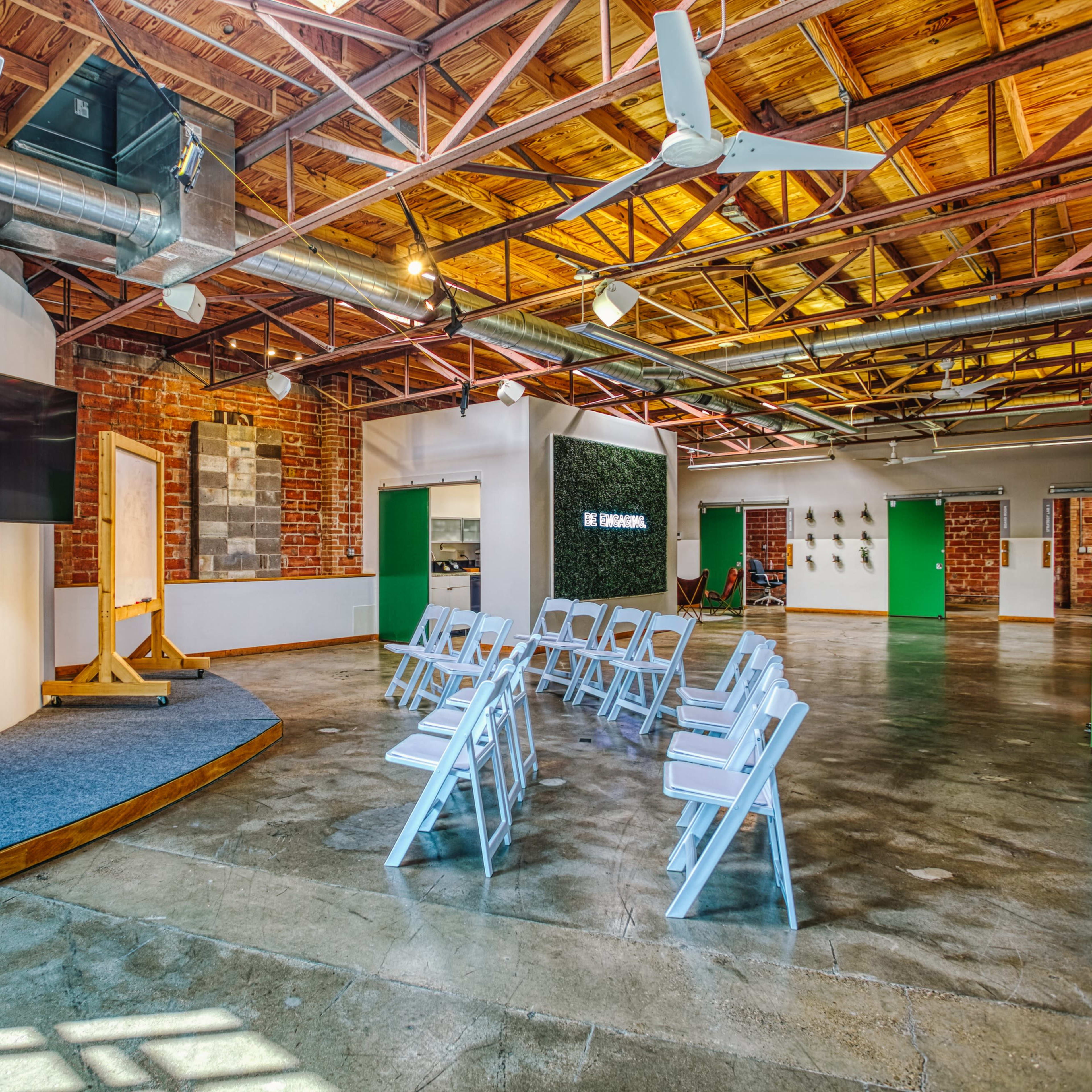 A spacious interior with wooden beams, featuring a presentation area with a screen and rows of white chairs arranged for an event.