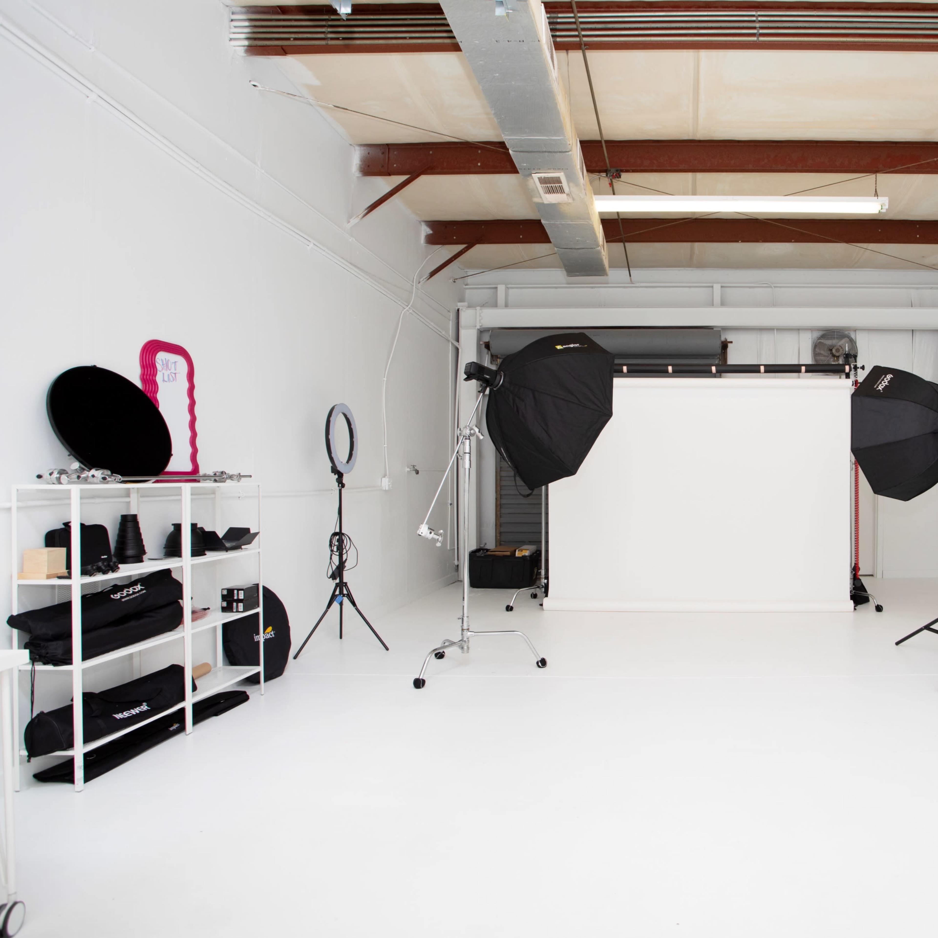 A photography studio with a white backdrop, lighting equipment, and various accessories organized on shelves.