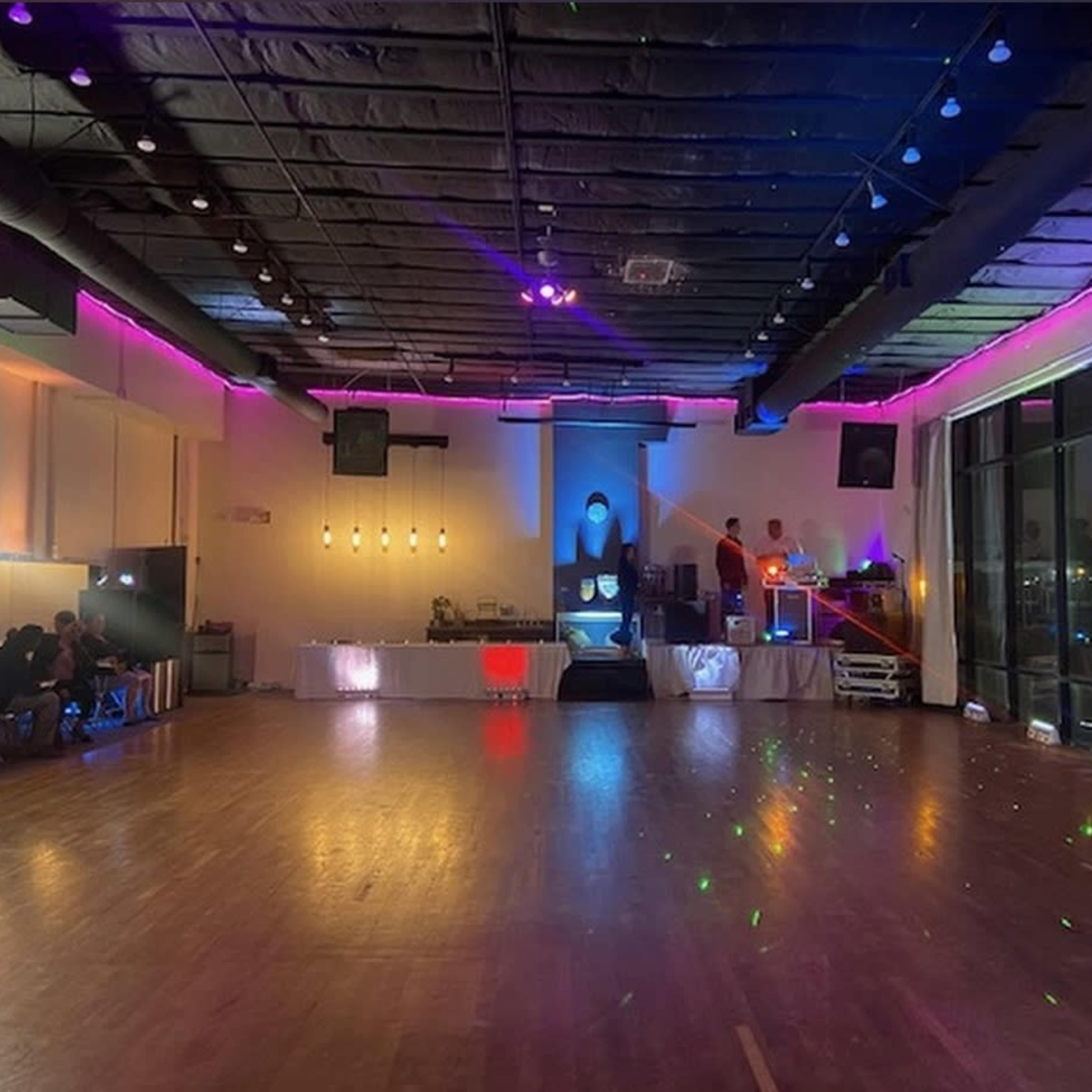 A spacious dance hall with colorful lights, a stage at the front, and seating along the side.