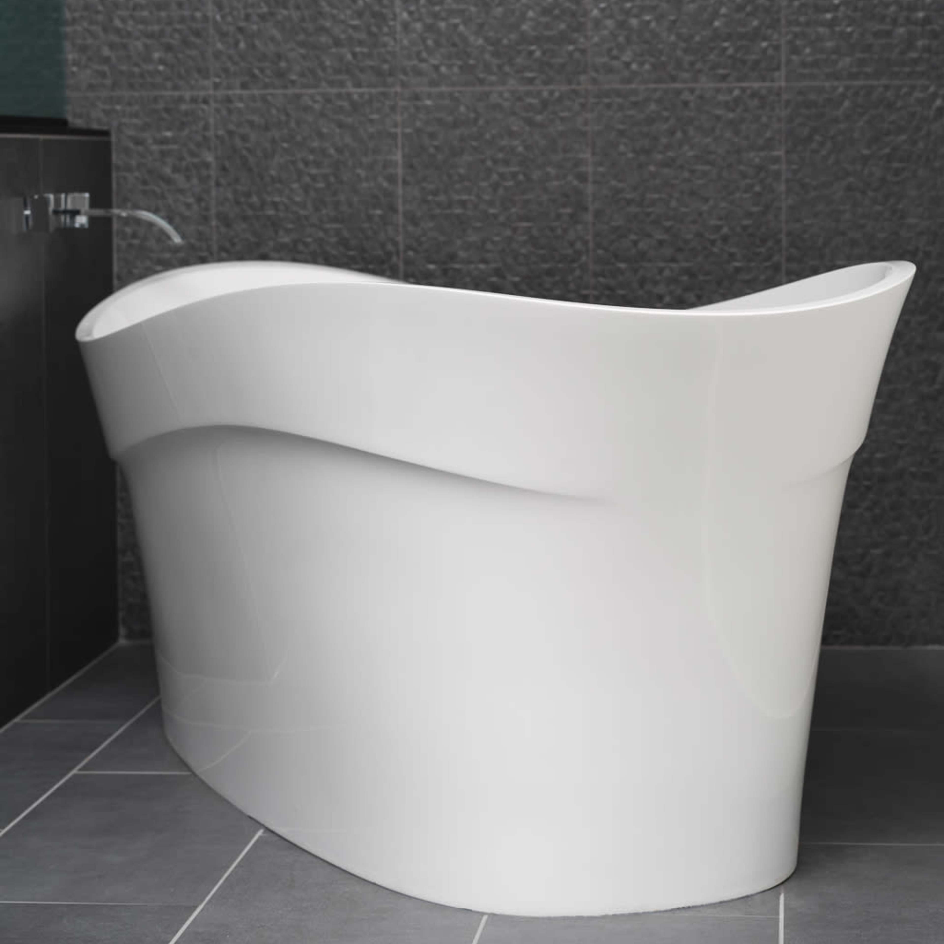 A modern white freestanding bathtub sits against a textured dark wall.