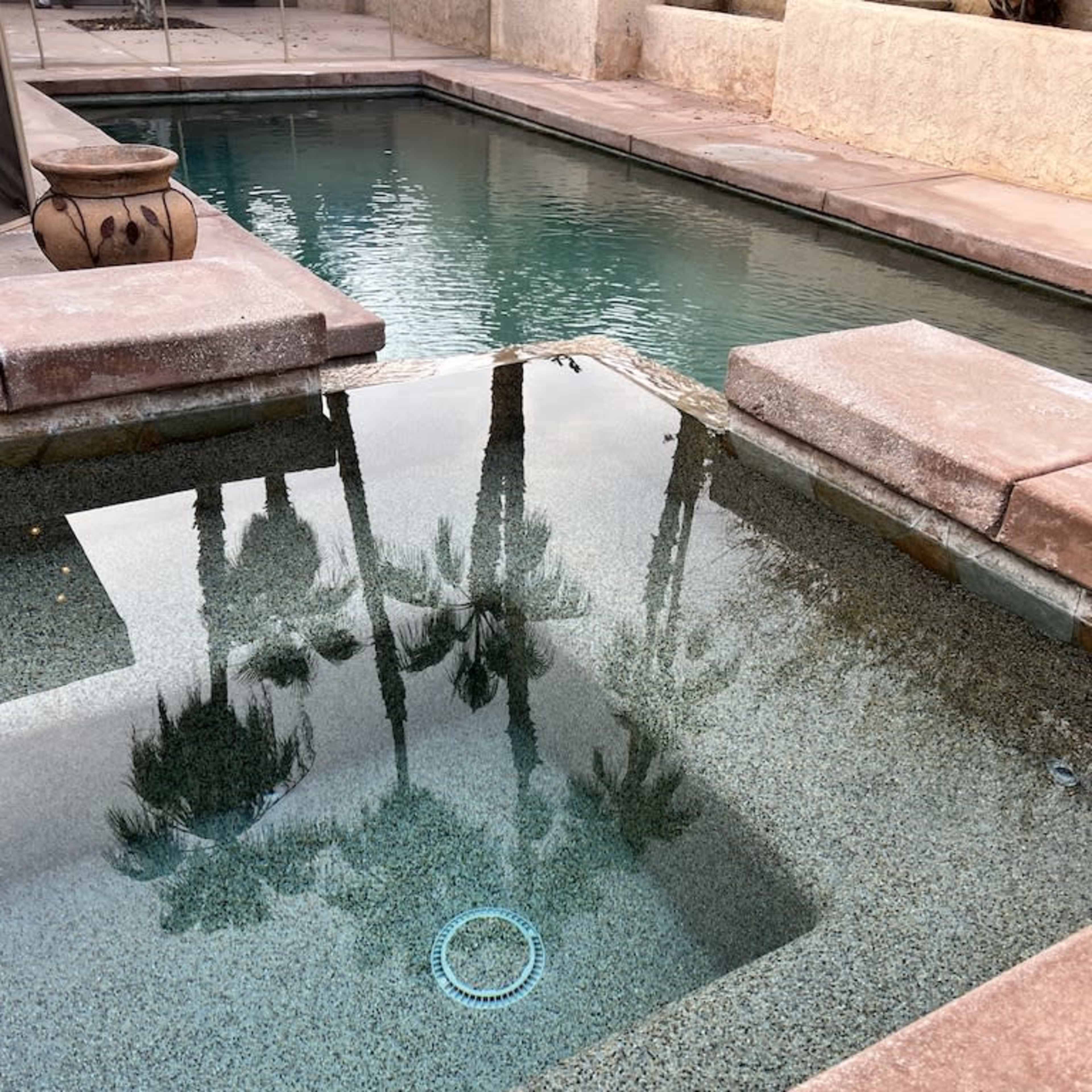 A still pool reflects palm trees and surrounds made of stone.