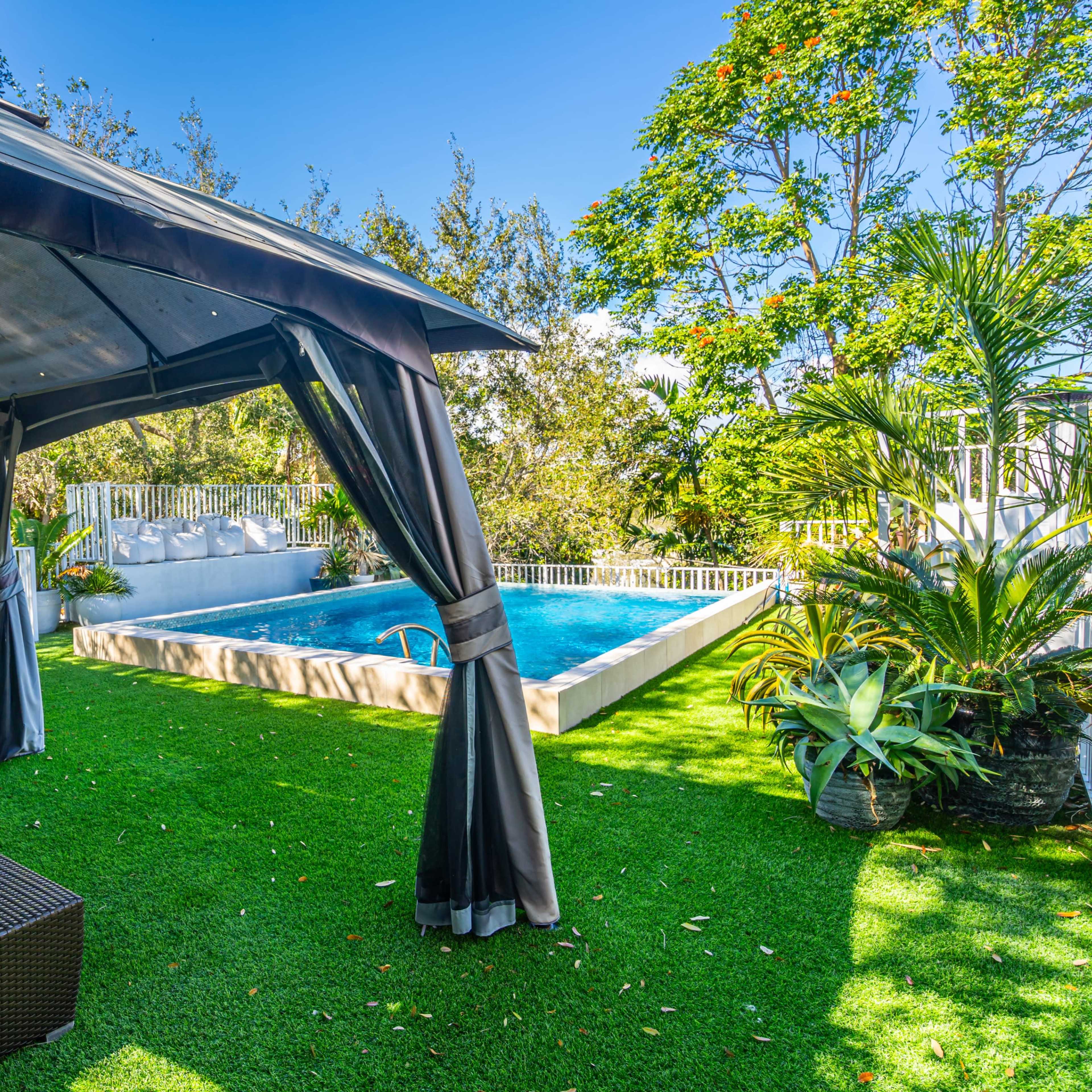 A patio area with outdoor seating next to a swimming pool surrounded by greenery.