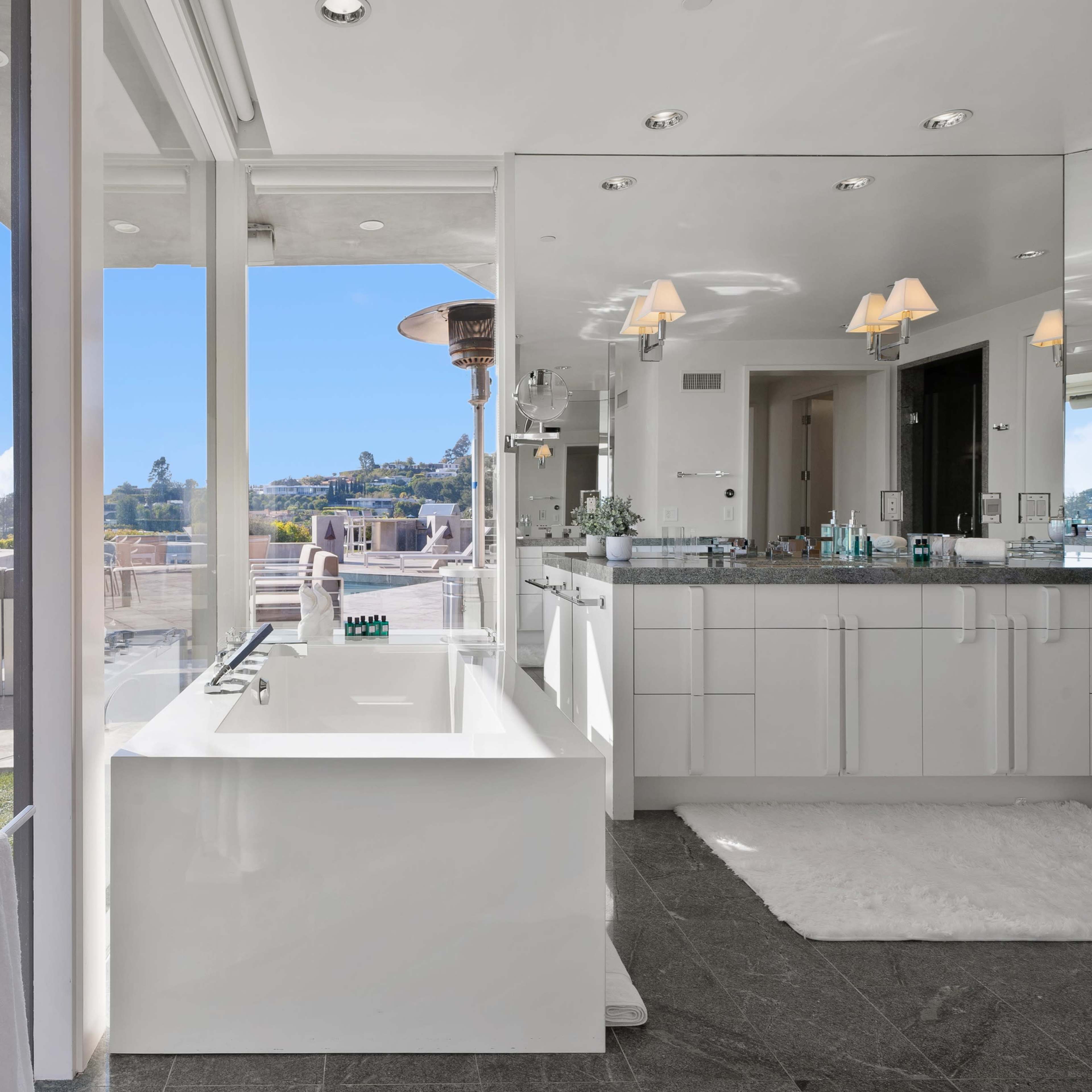 A modern bathroom with a freestanding bathtub and large windows offering a view of the outdoors.