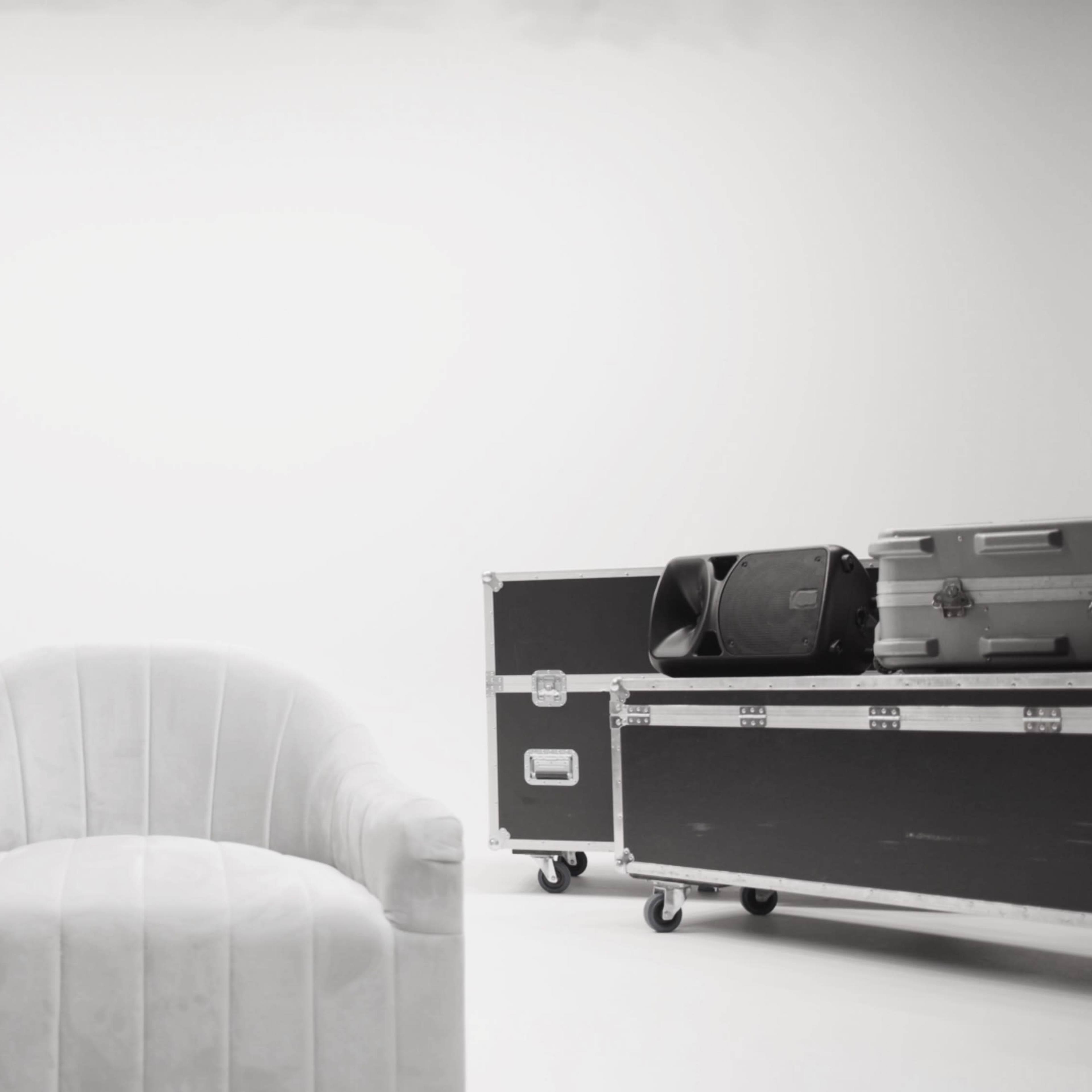 A single white chair is positioned between two black equipment cases in a minimalistic setting.