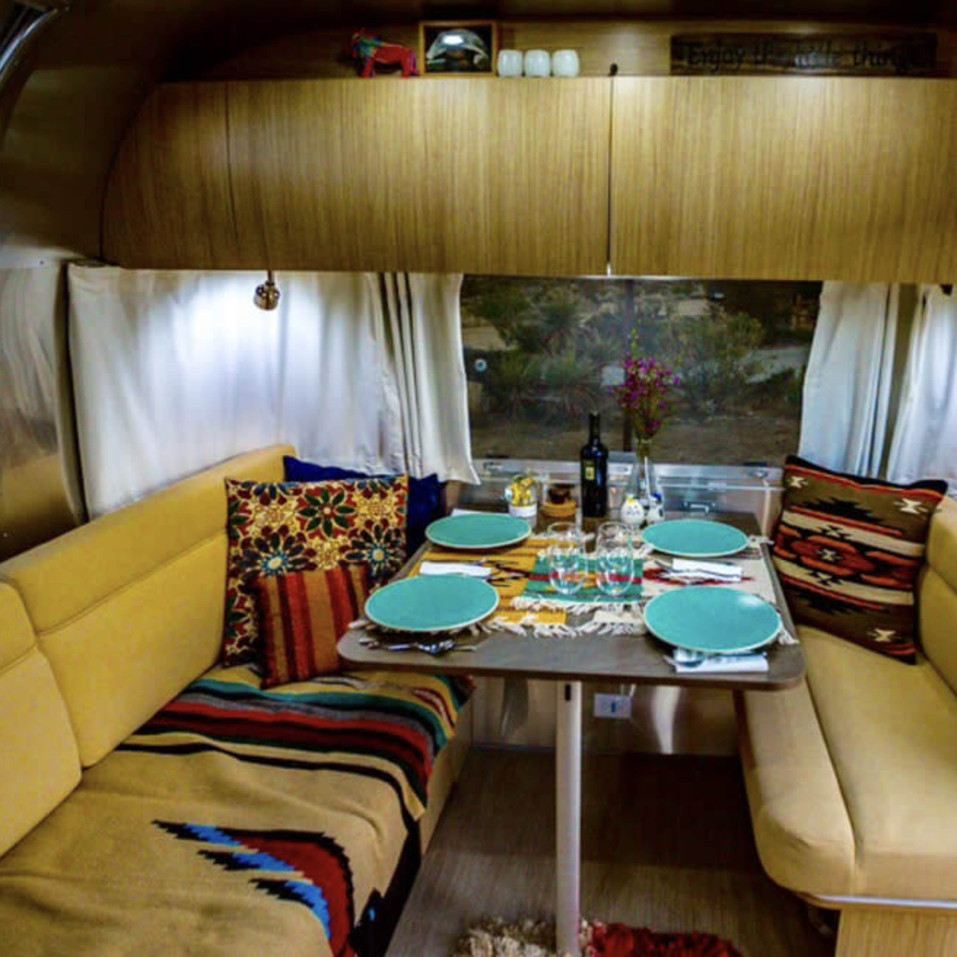 A cozy dining area inside a retro-style trailer, featuring a table set for a meal with colorful plates and decorative cushions.