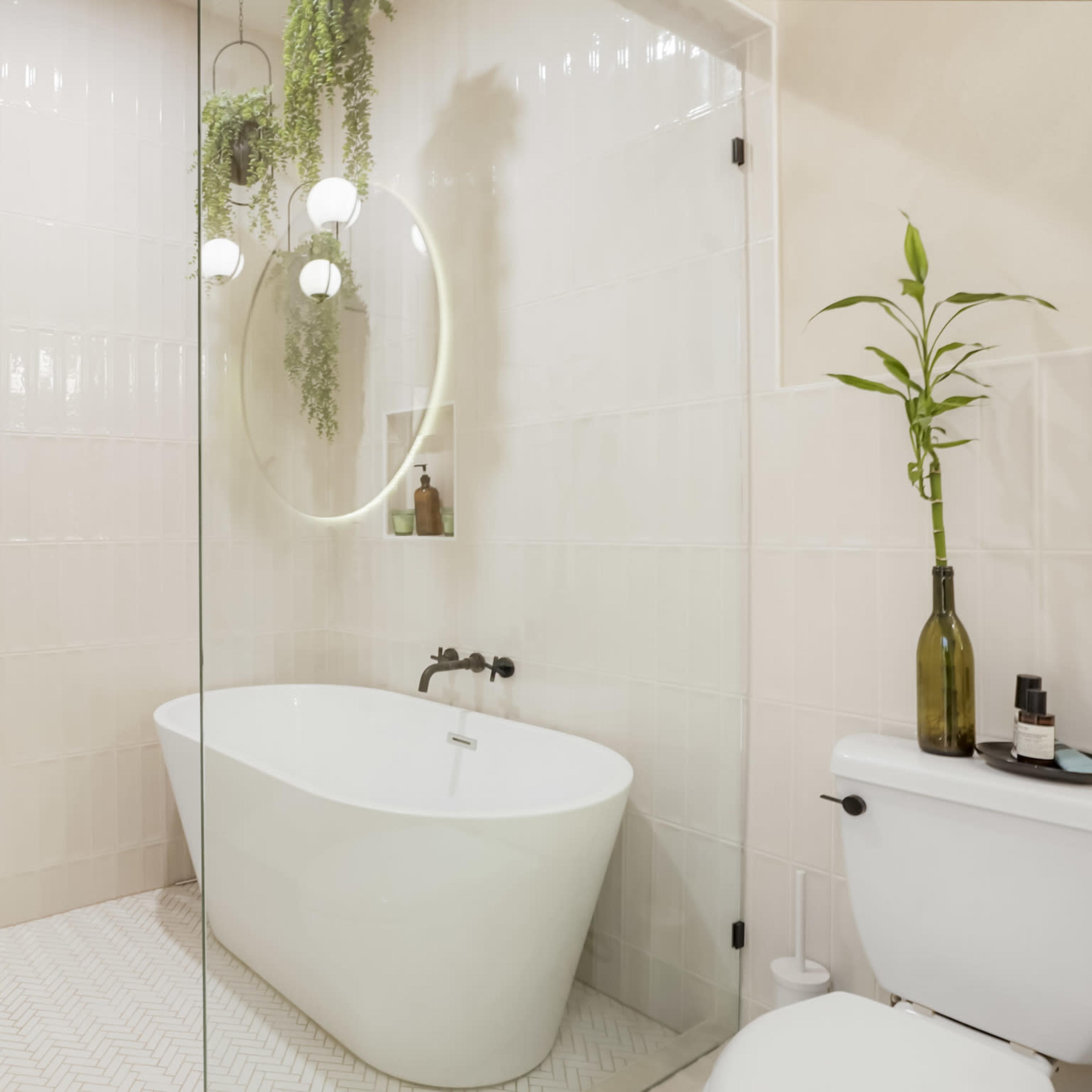 A modern bathroom featuring a freestanding white bathtub, a glass shower enclosure, and plants hanging from the ceiling.