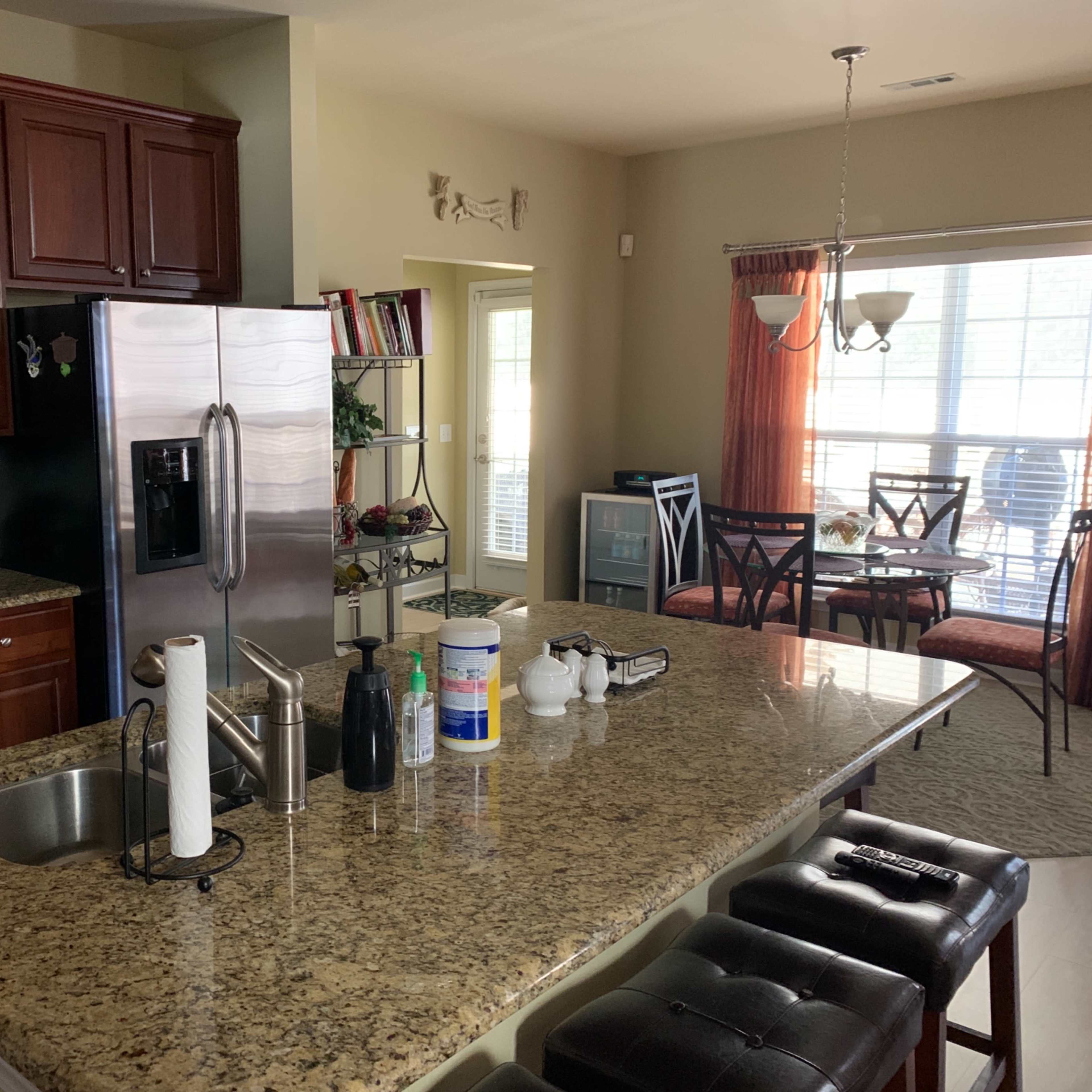 A kitchen with wooden cabinets, a granite countertop, and modern appliances, connected to a dining area with large windows.