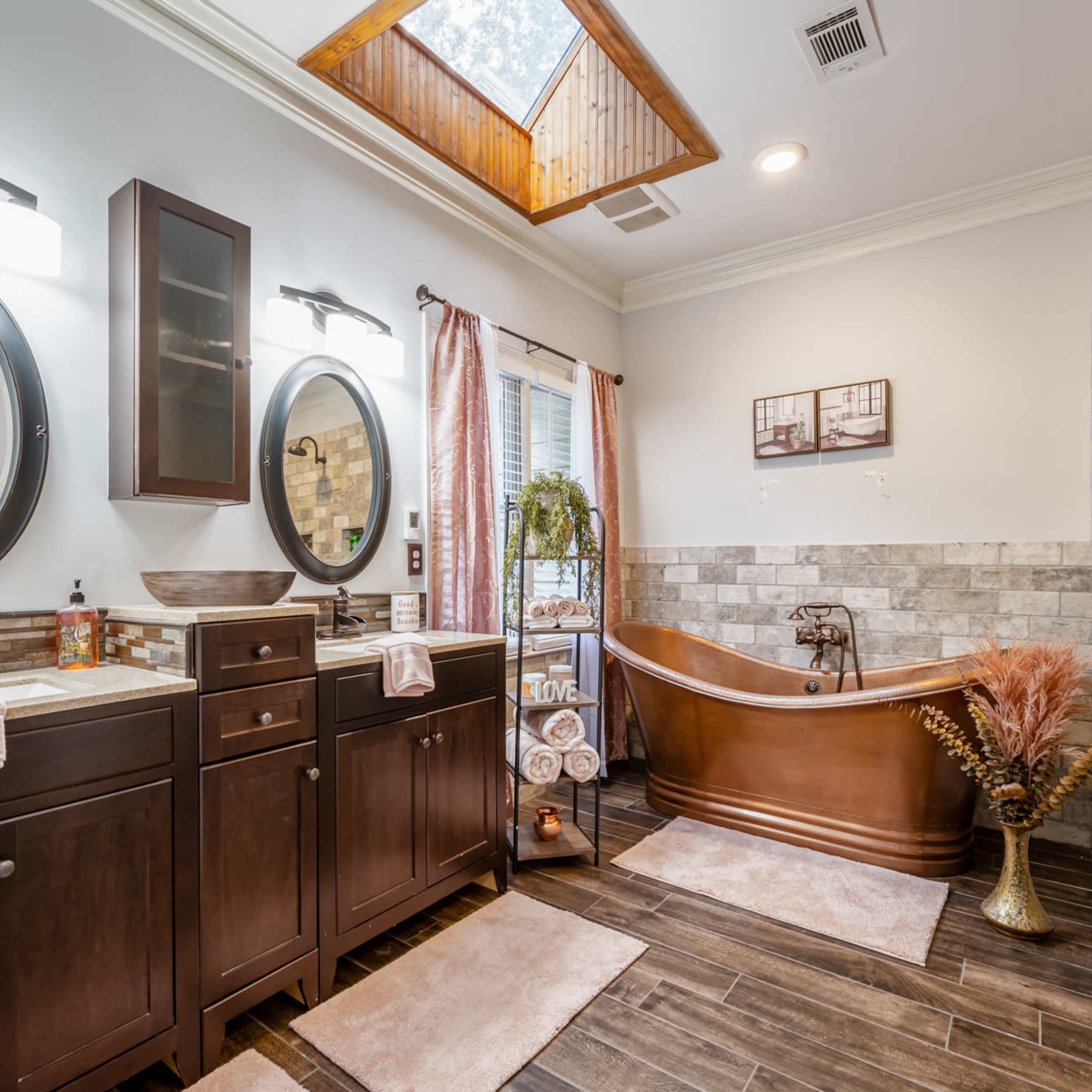 A modern bathroom featuring dual sinks, a freestanding bathtub, and natural light coming through a skylight.
