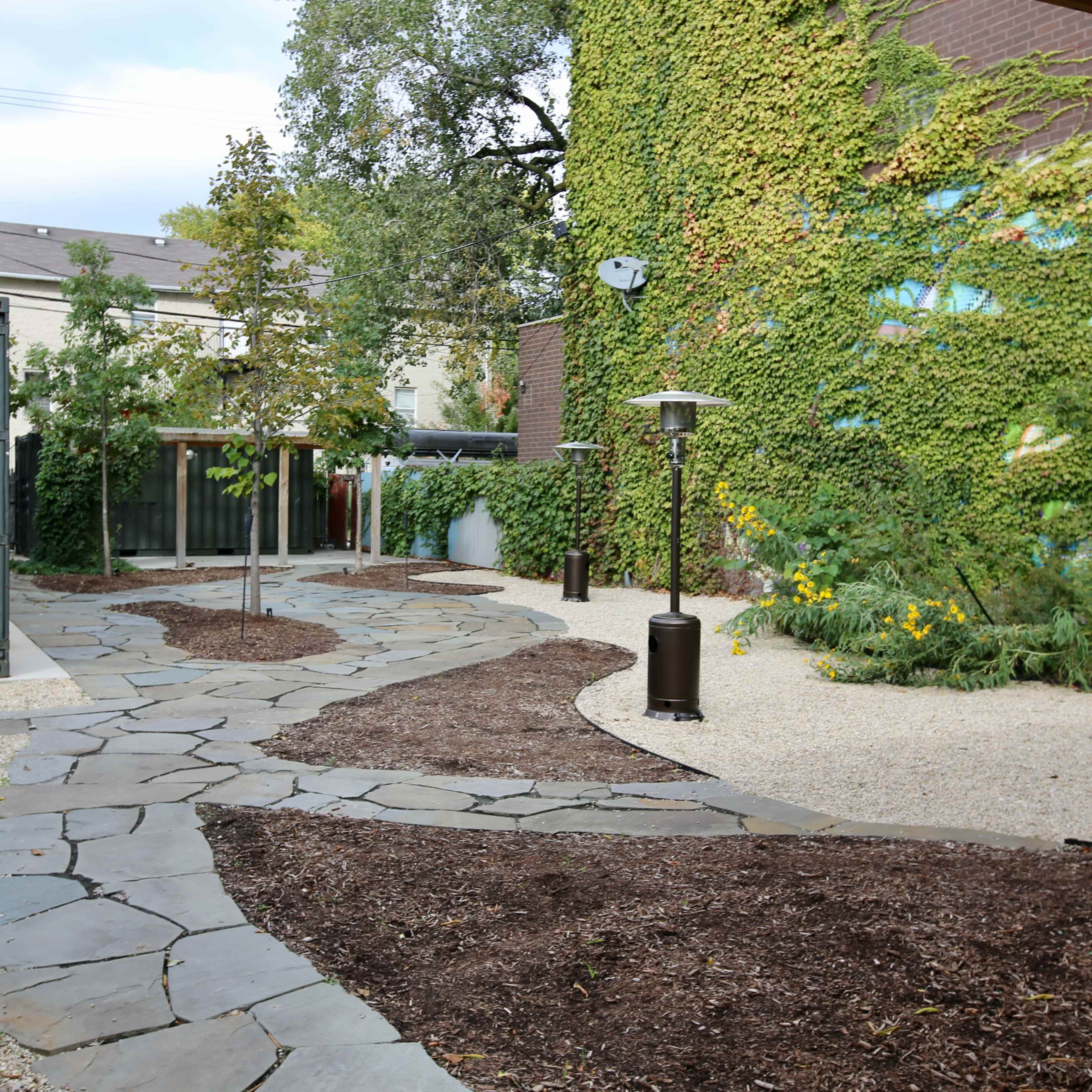 A landscaped garden area featuring a stone pathway winding through gravel, bordered by greenery and decorative plants.