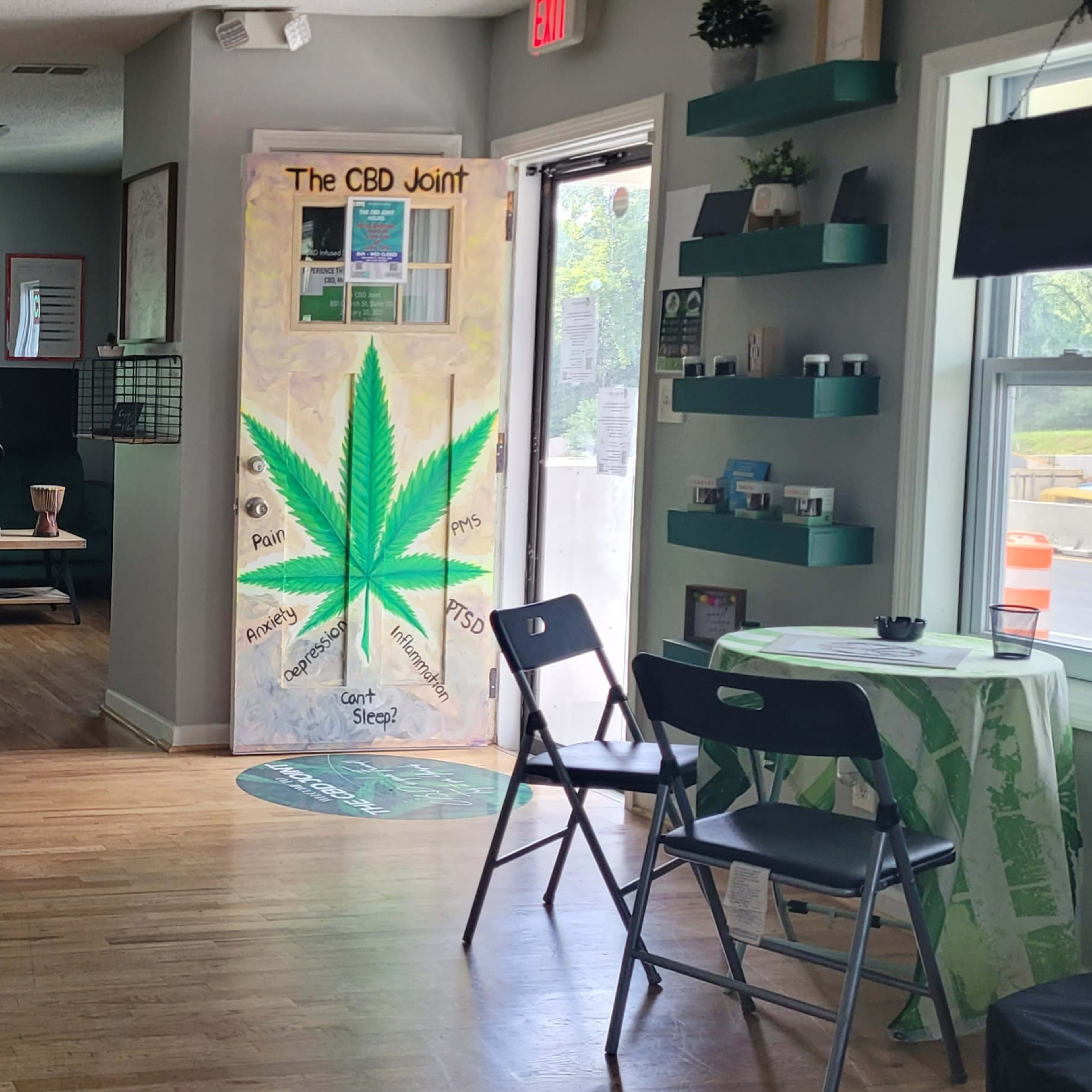 An interior space featuring a seating area, an empty easel, and a prominent green cannabis leaf mural on the wall.