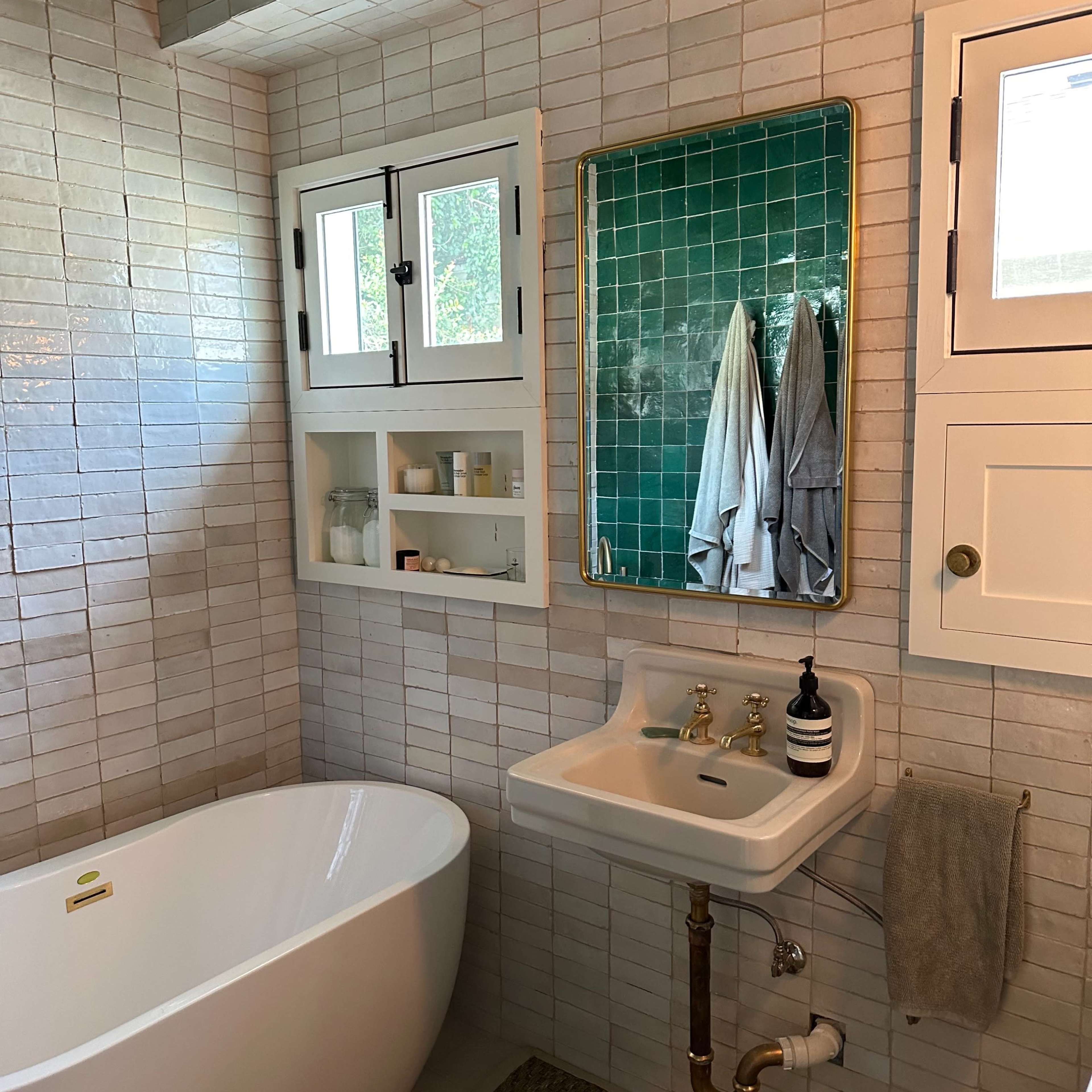 A modern bathroom featuring a freestanding bathtub, a small sink with a mirror, and wall tiles in light and dark shades.
