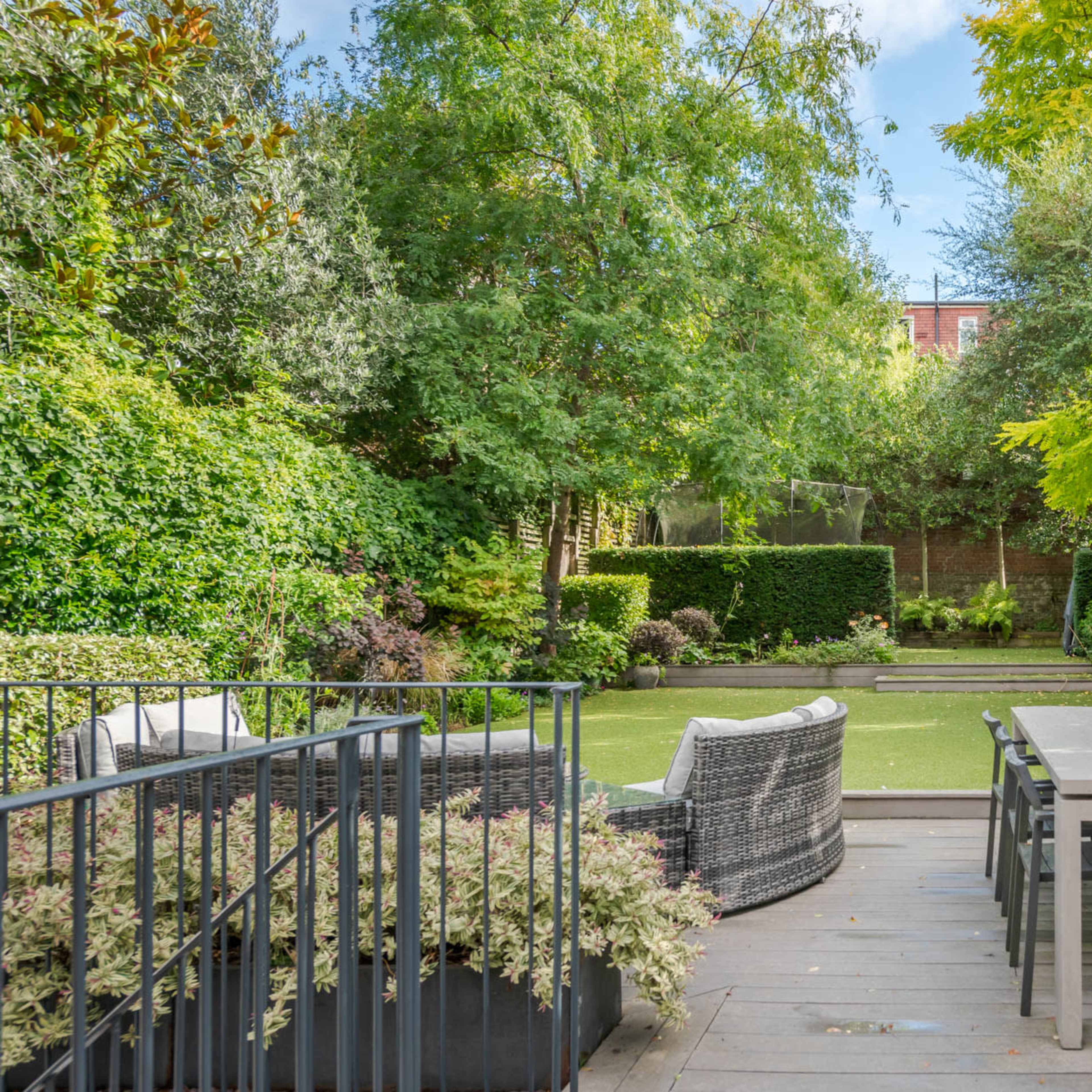A well-maintained garden features a spacious dining table and chairs, surrounded by lush greenery and trimmed hedges.
