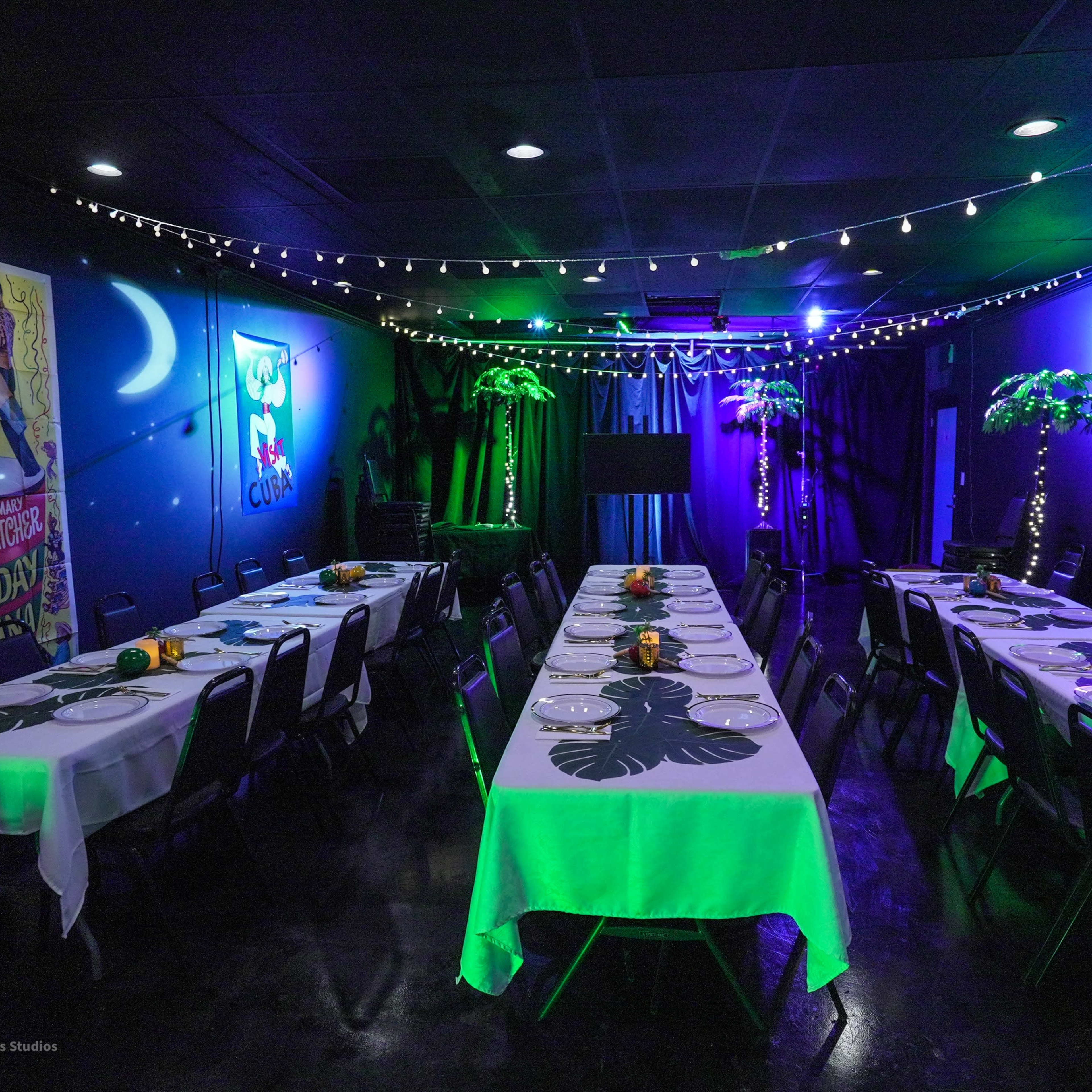 A decorated dining area with long tables set for a festive event, featuring lights, tropical-themed decorations, and posters on the walls.