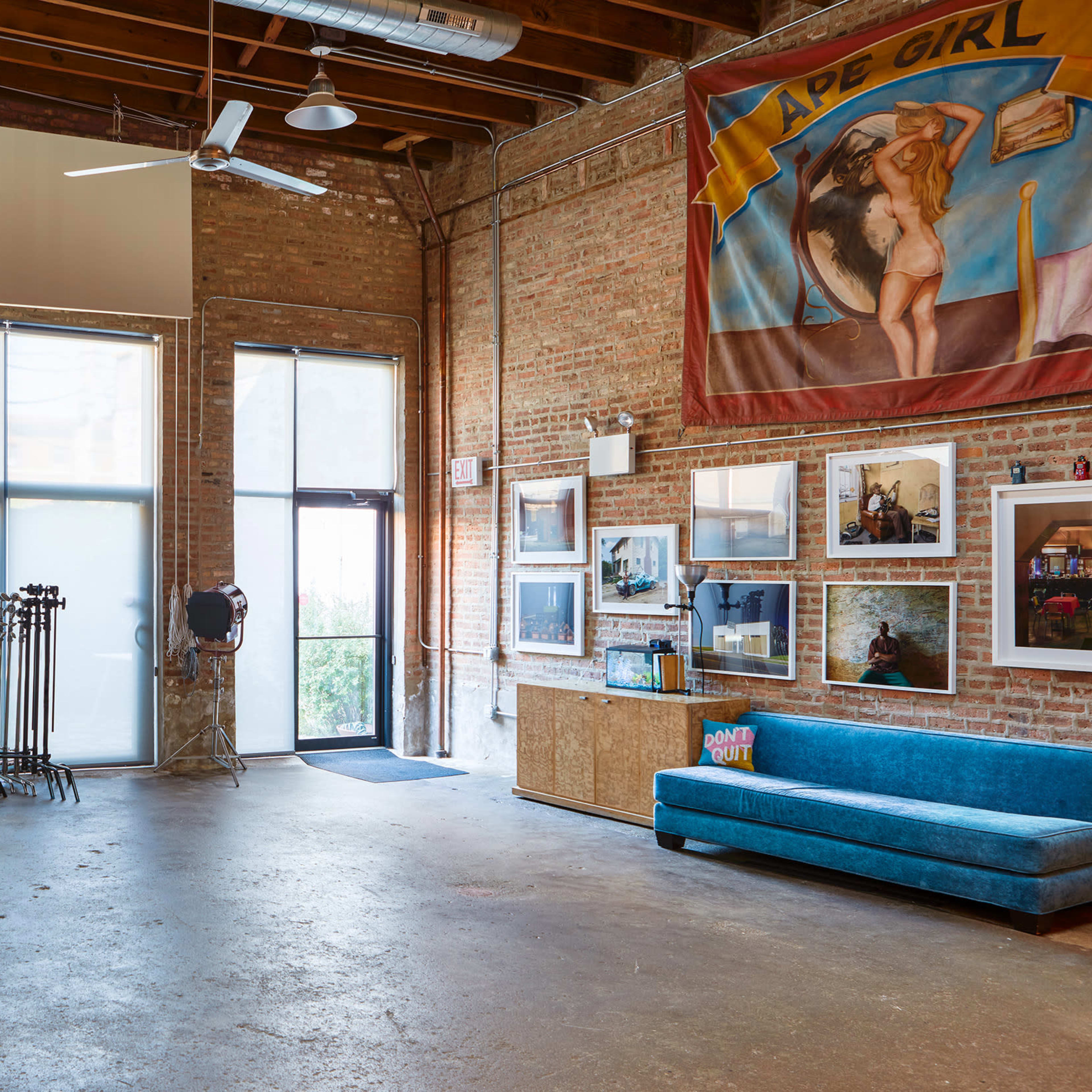 A spacious studio with exposed brick walls, large windows, and various artworks displayed on the walls, including a large banner.