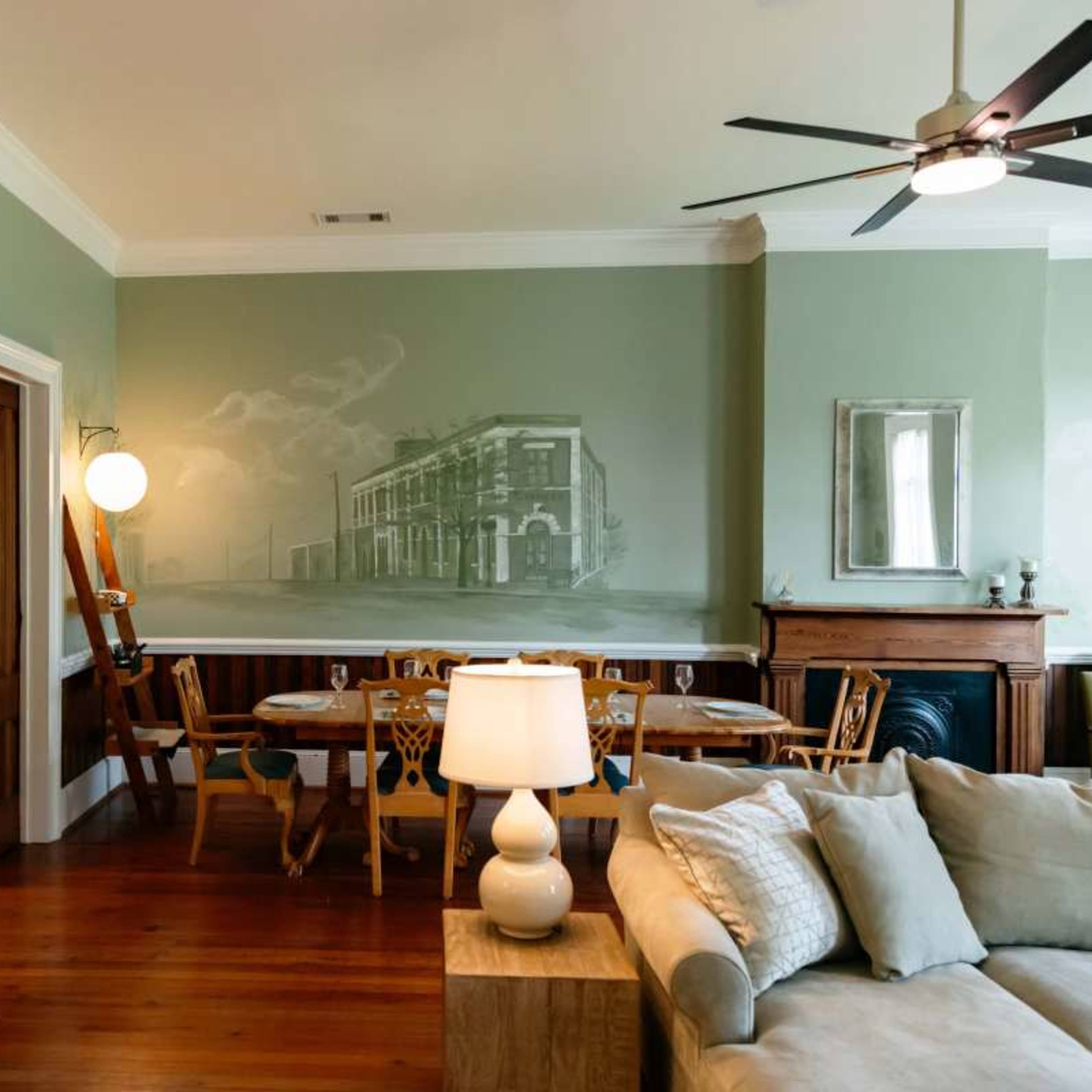 A stylish interior living space featuring a mural on the wall, a dining area with wooden furniture, and a cozy seating area with a light-colored sofa and a table lamp.