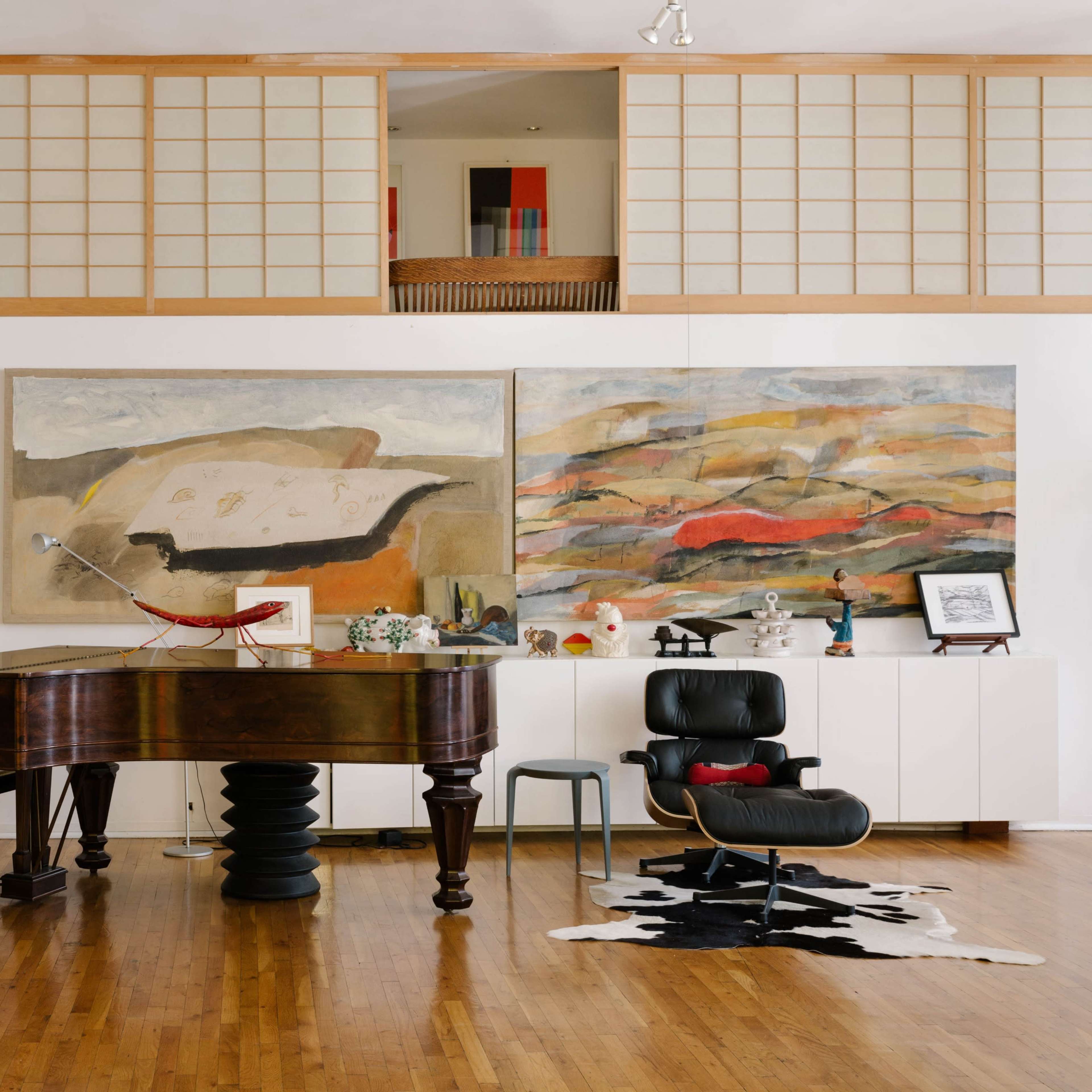 A spacious room featuring a grand piano, two large abstract paintings on the wall, and a modern chair with a patterned rug on the hardwood floor.