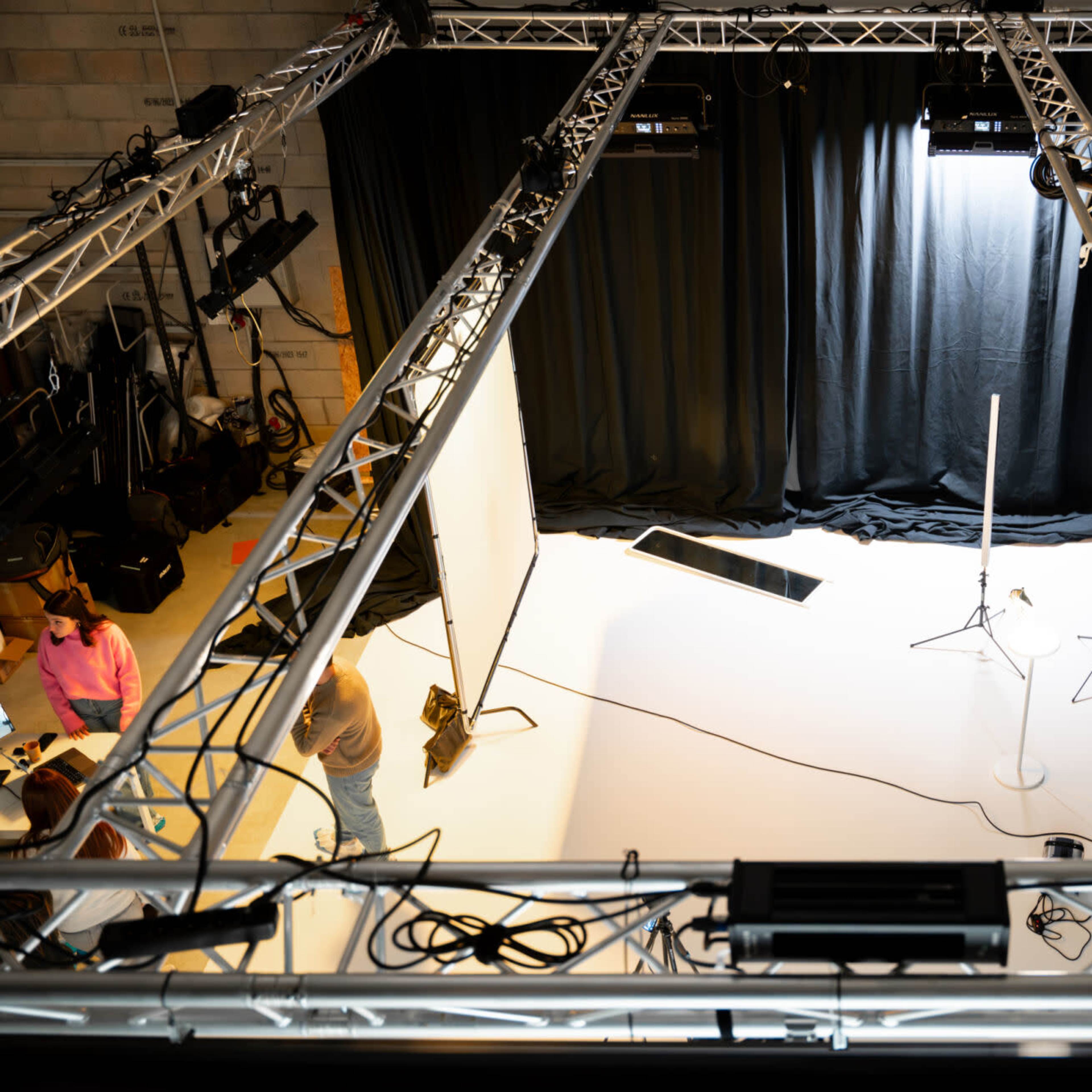 An overhead view of a studio setup featuring a white backdrop, lighting equipment, and a grid of truss framing the space.