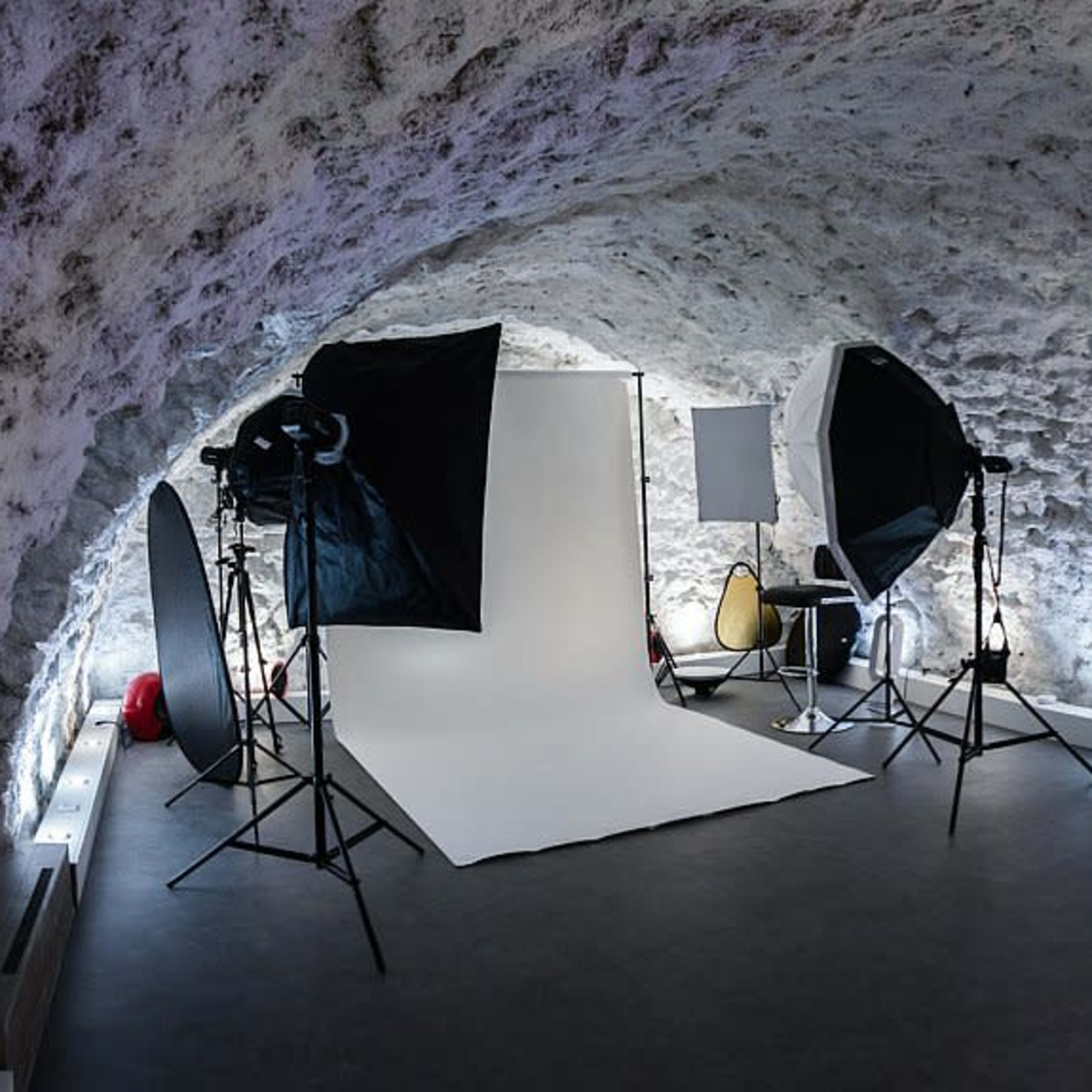 A photography studio with a white backdrop, lighting equipment, and various props in a stone-walled room.