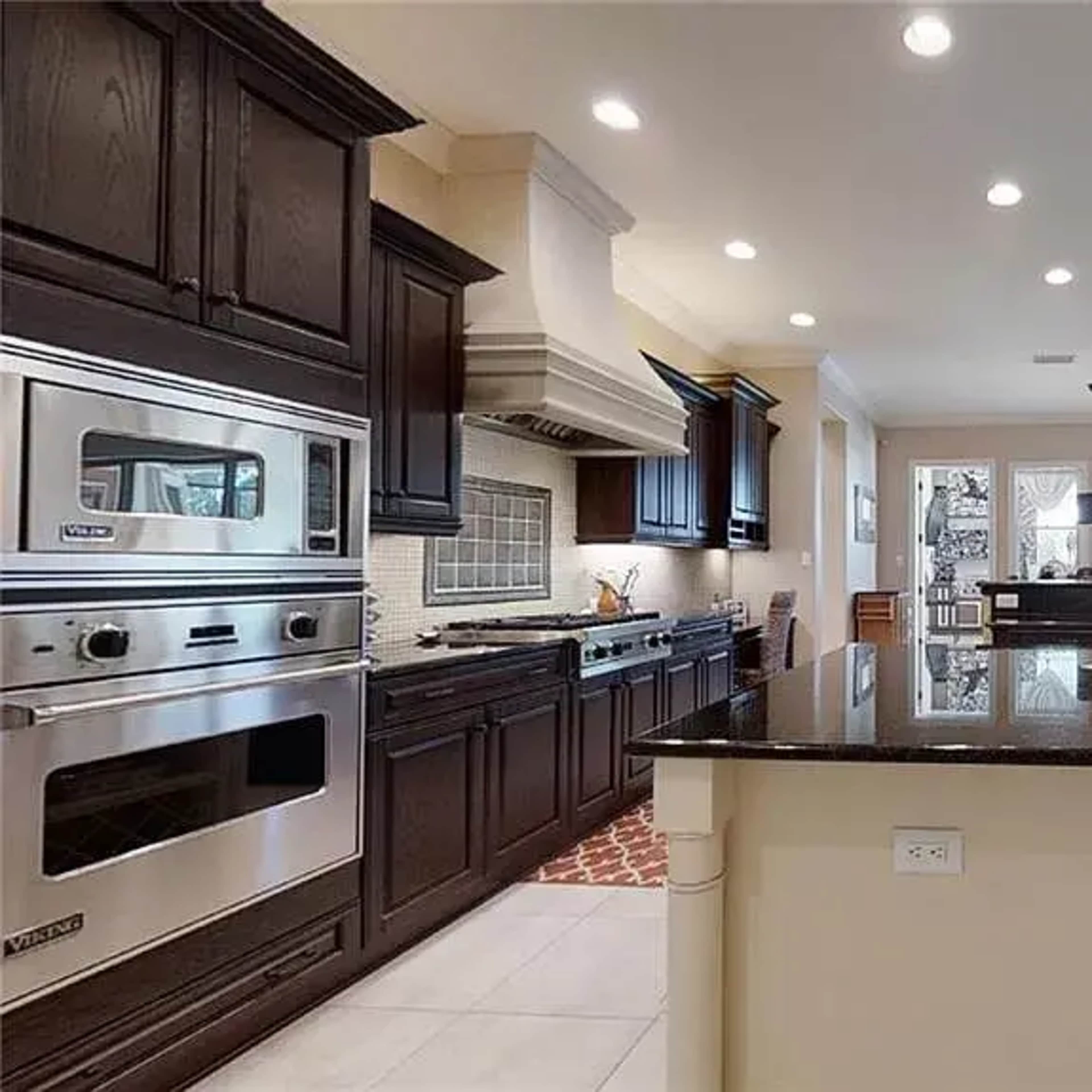 A spacious kitchen with dark wooden cabinetry, a large island with a black countertop, and modern appliances.