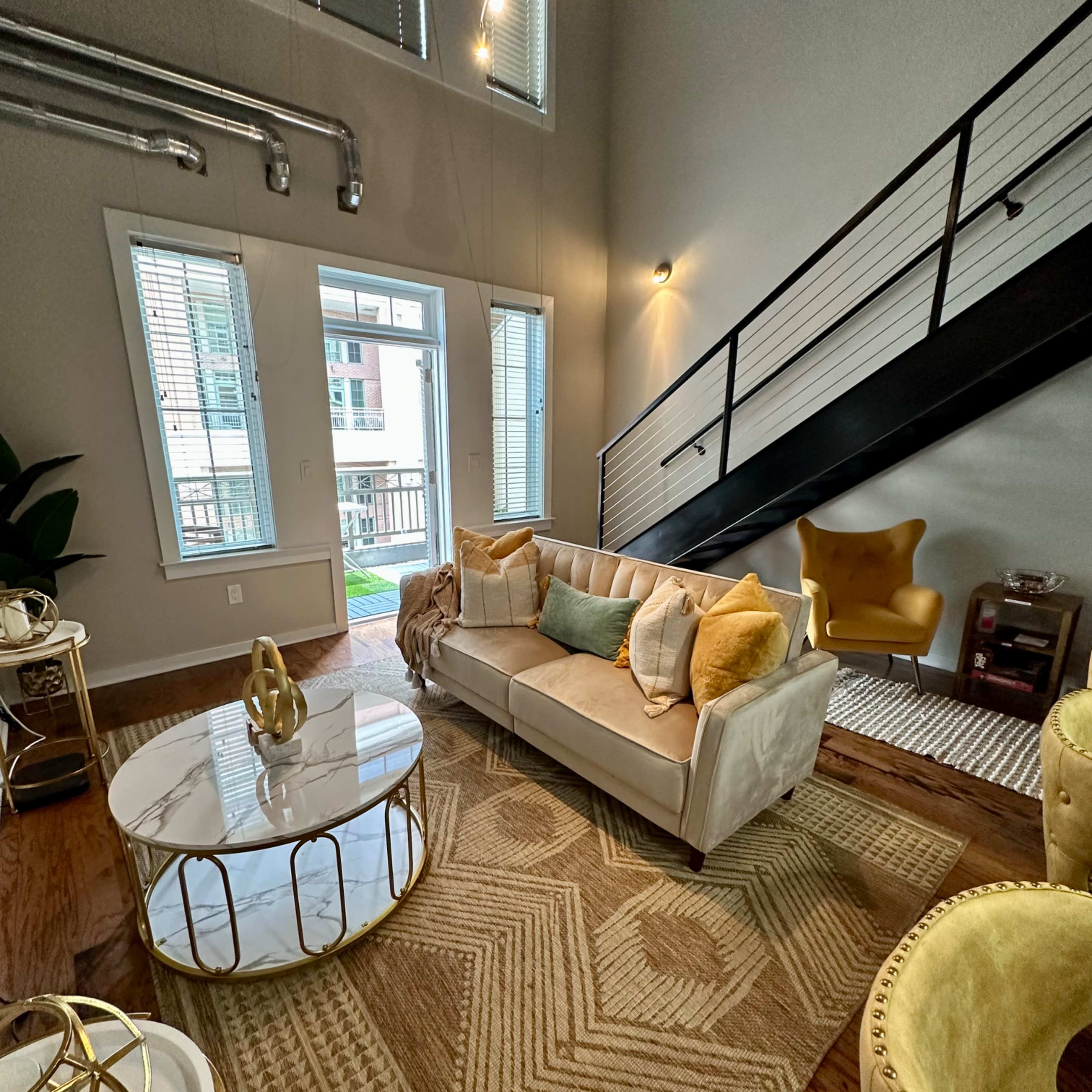 A modern living room featuring a light-colored sofa with decorative pillows, a round coffee table, and a staircase leading to an upper level.