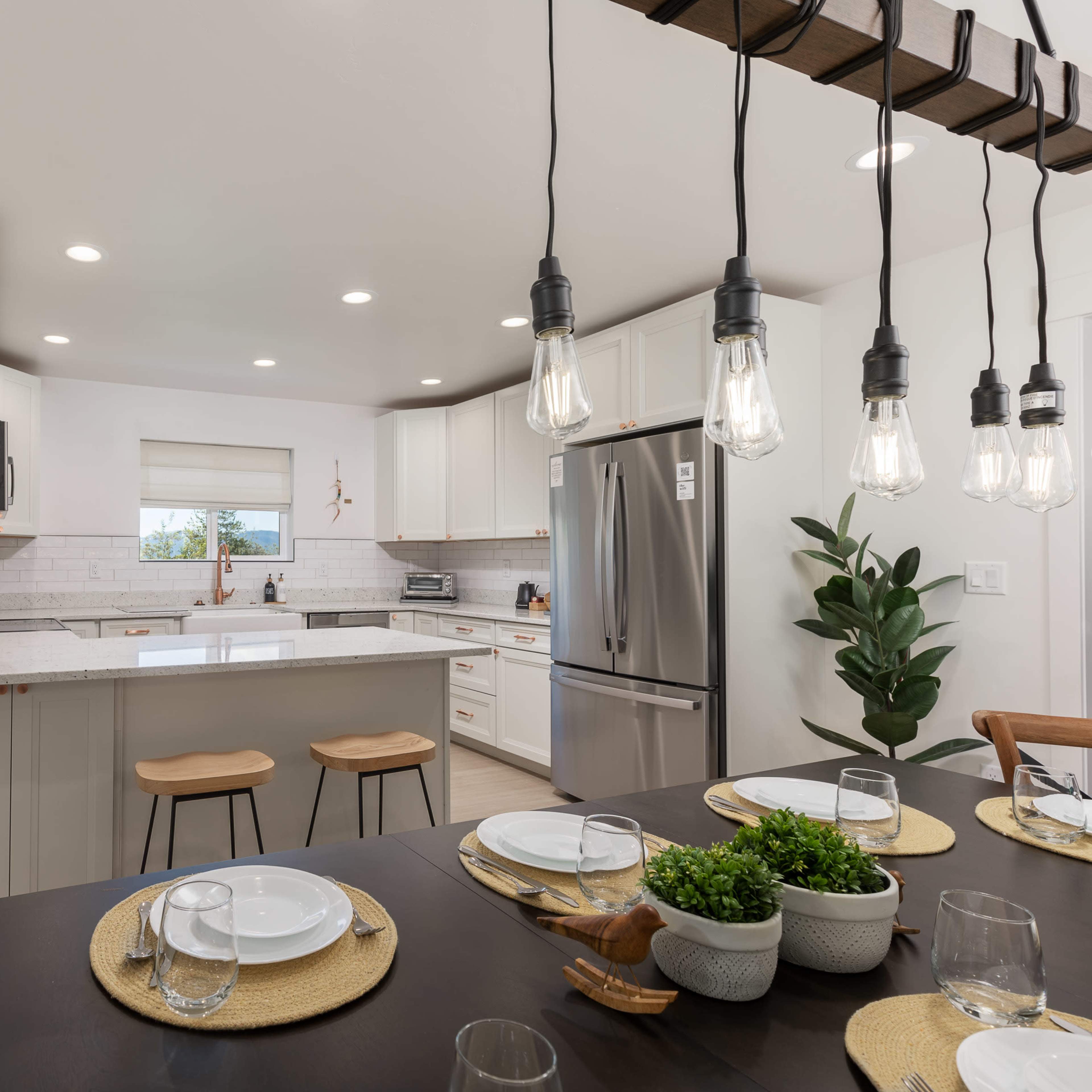 A modern kitchen with white cabinetry, a central island with bar stools, and a dining table set for a meal.