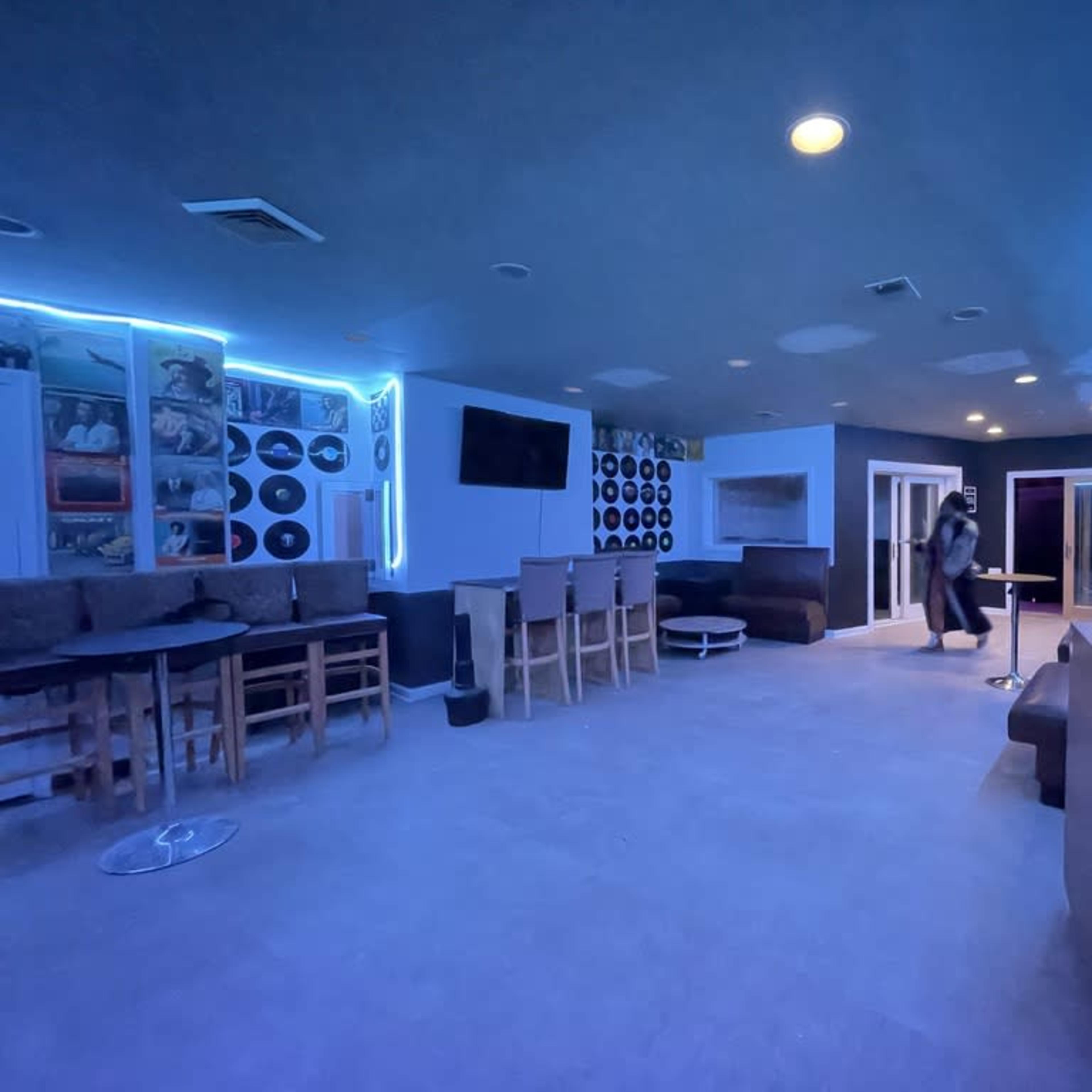 A dimly lit lounge area features wooden seating, vinyl records on the walls, and blue LED lighting.