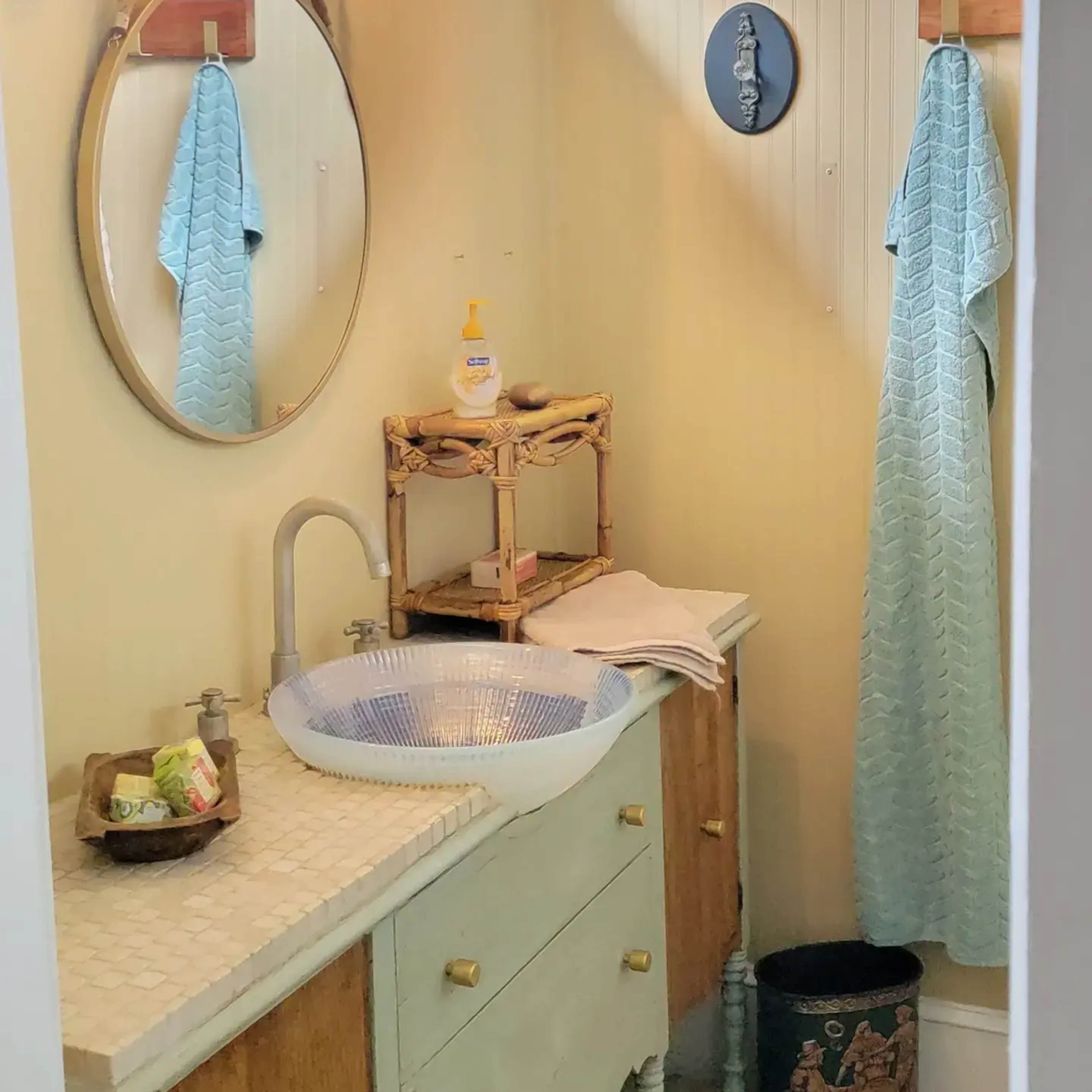 A small bathroom with a circular mirror, a sink atop a two-tone cabinet, a chandelier, and two light blue towels hanging on the wall.