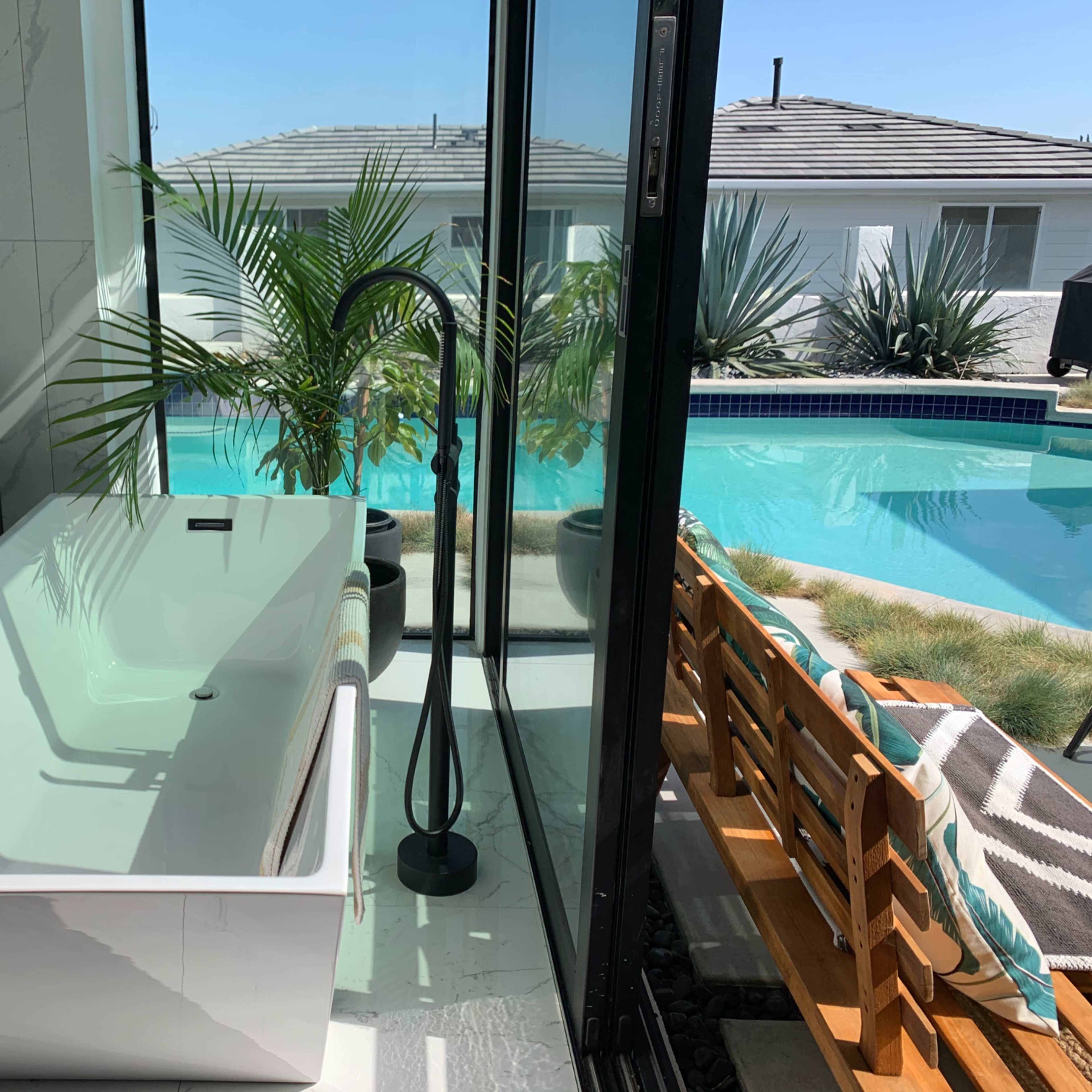 A modern house features a clean, rectangular pool surrounded by concrete patios and large windows, with a spiral staircase leading to a roof deck.