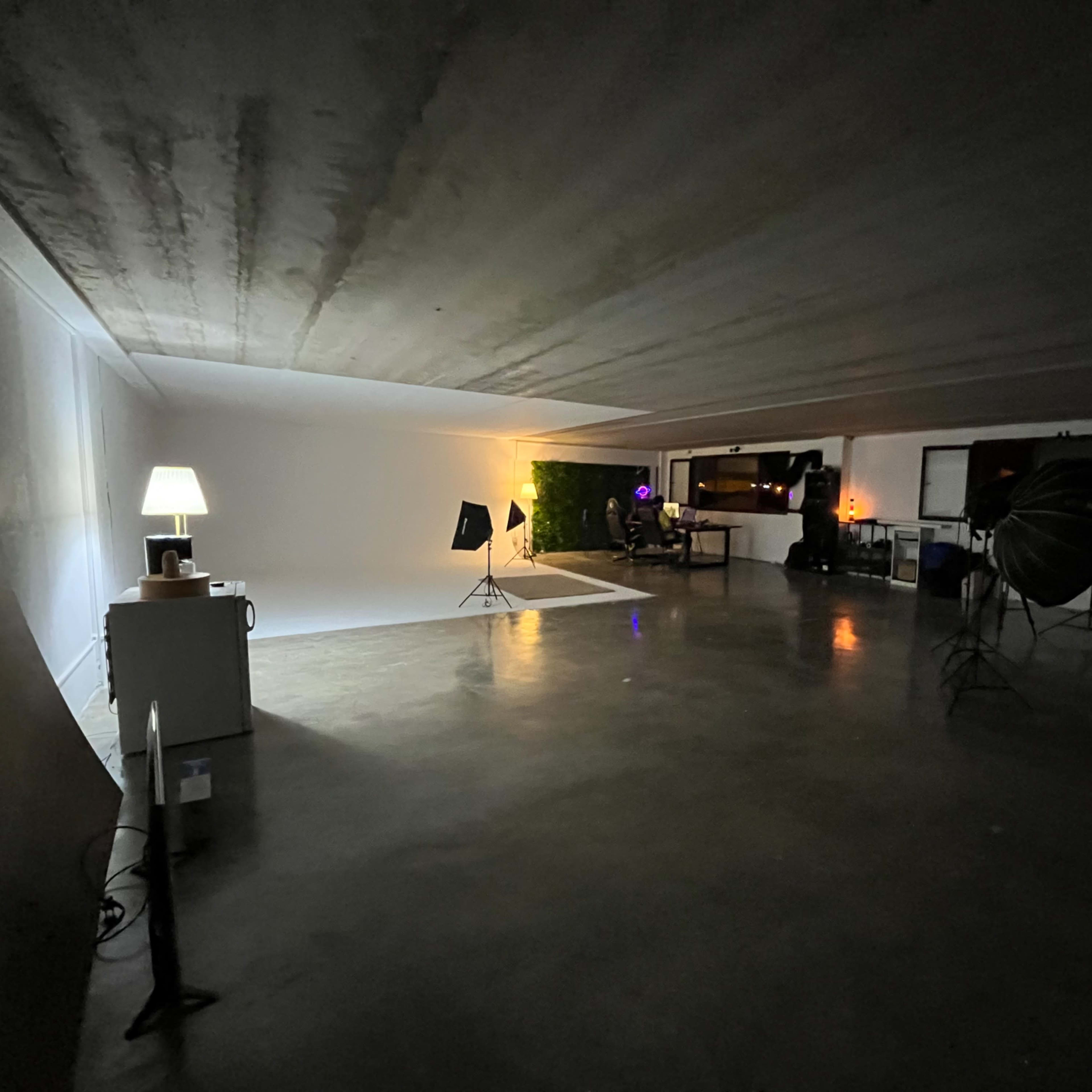 A spacious photography studio with a white backdrop, lighting equipment, and a large window reflecting a dimly lit area.