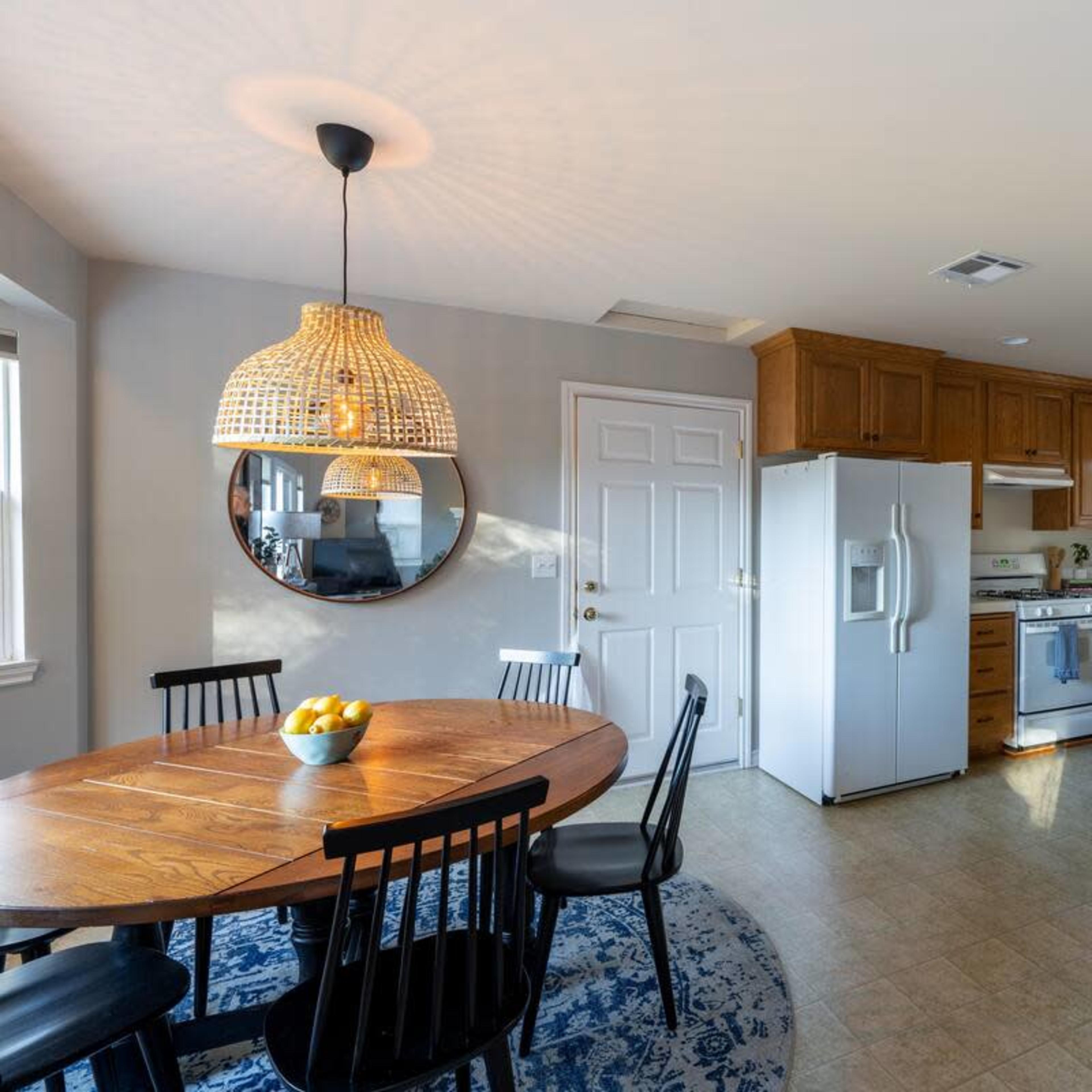 A kitchen features wooden cabinets, a round dining table with black chairs, a large refrigerator, and a patterned rug under the table.