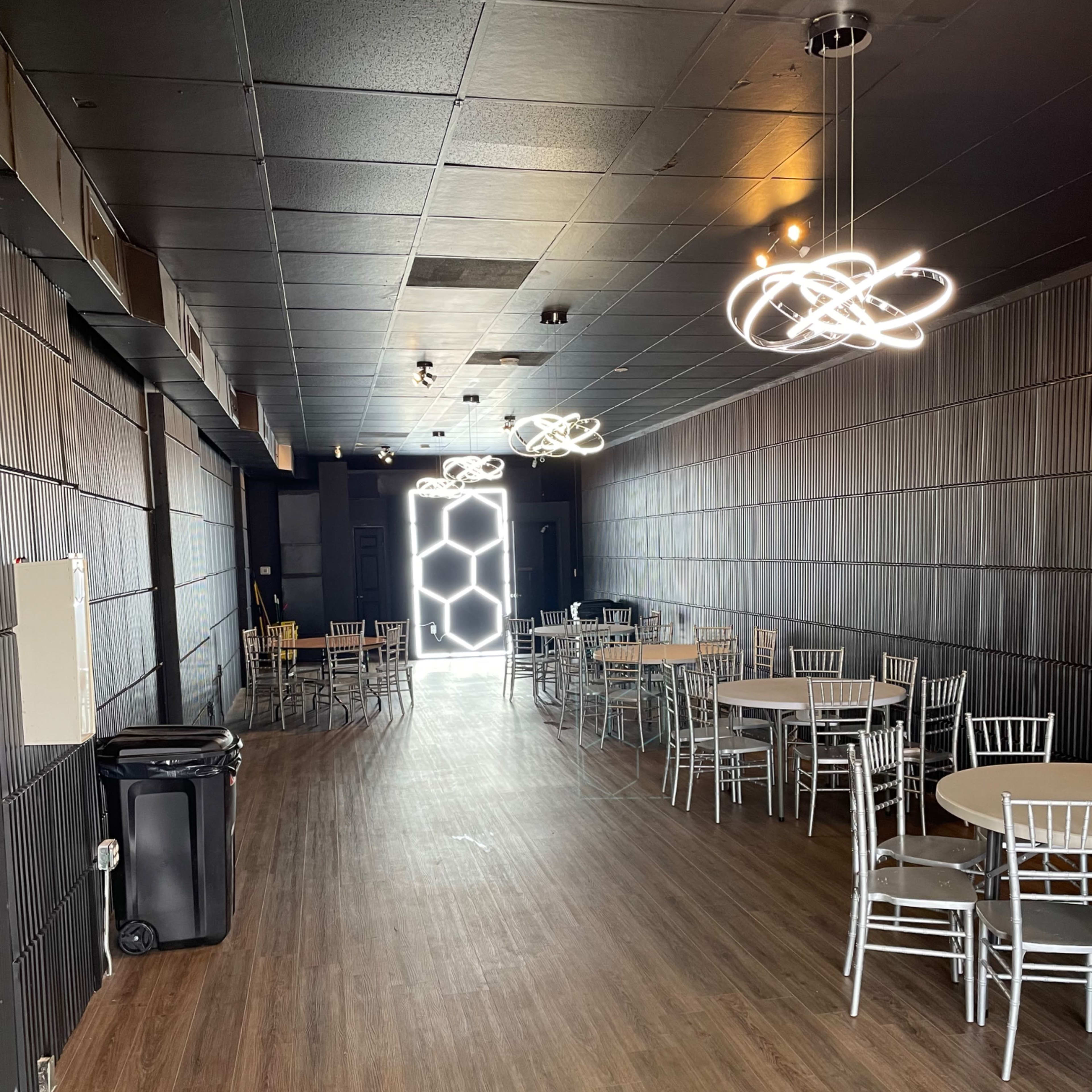 A spacious, empty indoor event room with several round tables and modern light fixtures.