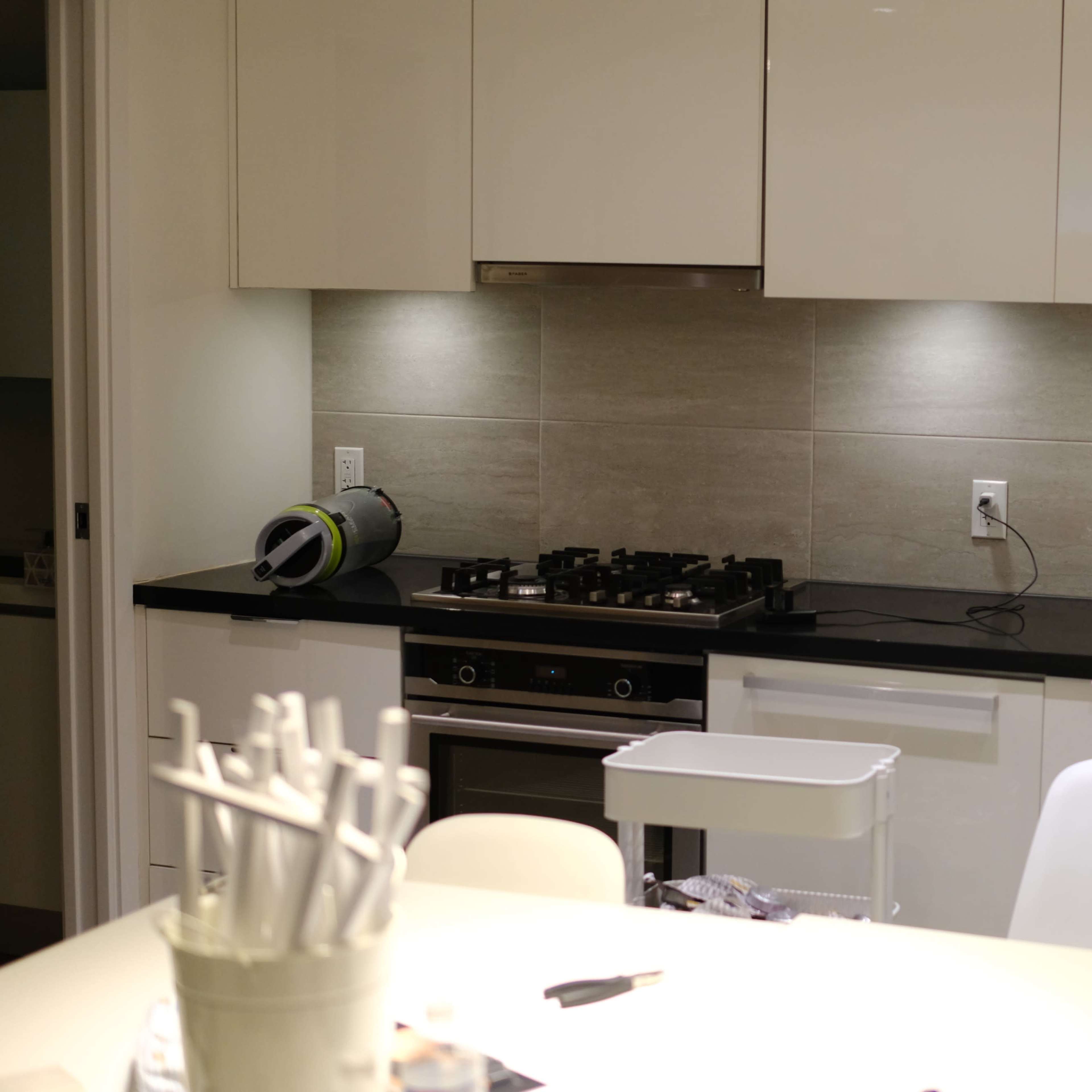 A modern kitchen with a gas stove, a stainless steel sink, and sleek cabinetry illuminated by under-cabinet lighting.