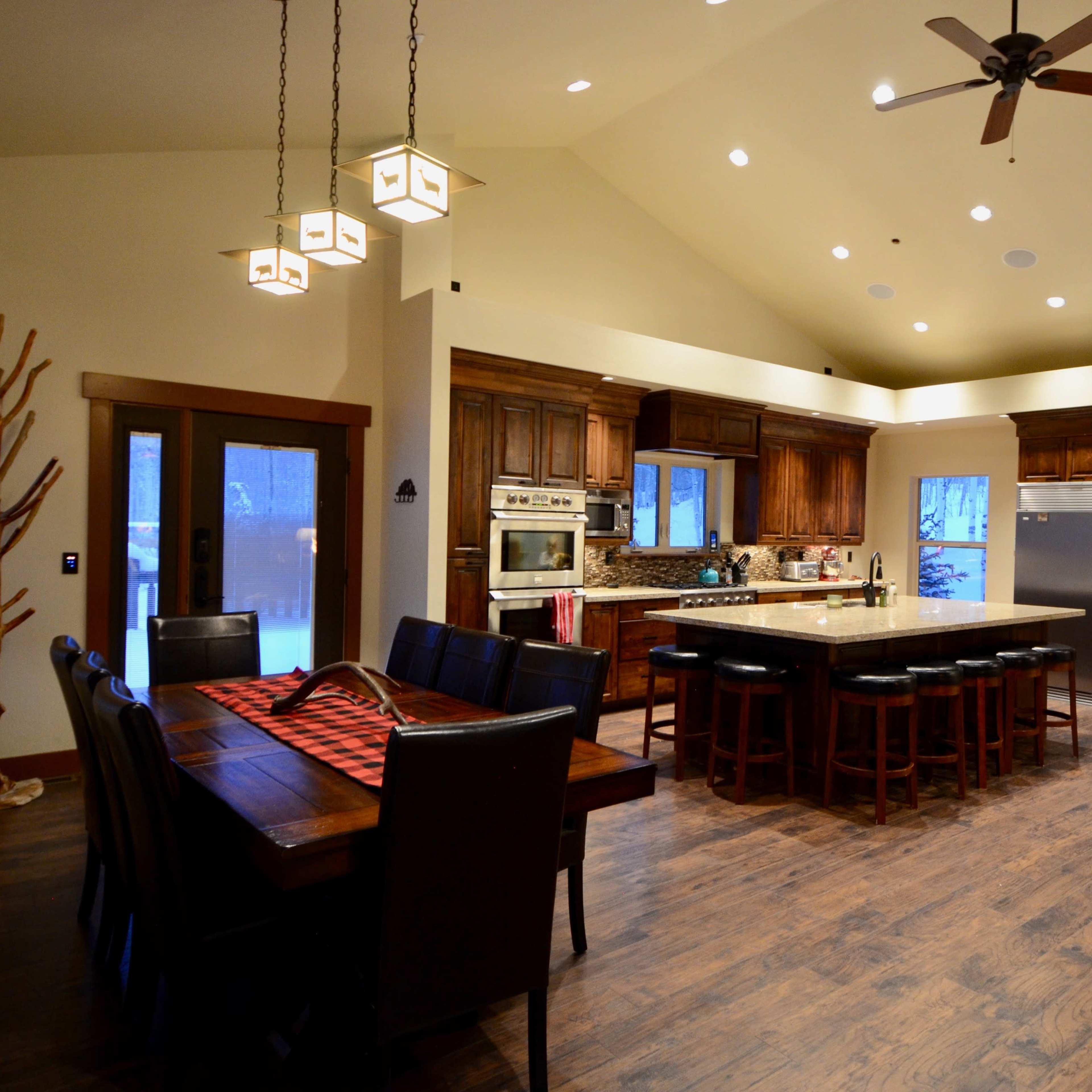 A spacious kitchen and dining area featuring wooden cabinets, a large island with seating, and a dining table with a checkered tablecloth.