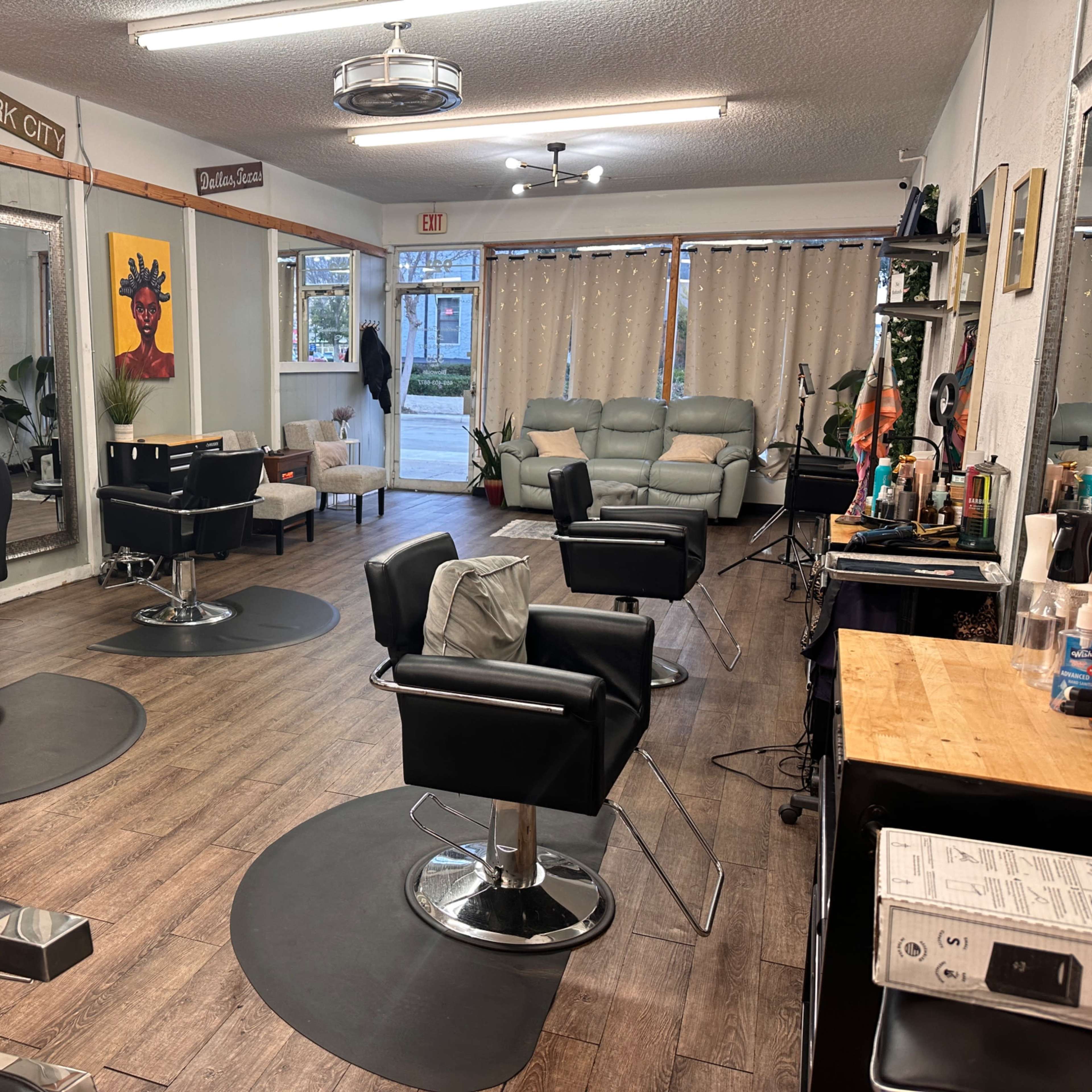 The interior of a hair salon features several styling chairs, mirrors, and a waiting area with a couch and artwork on the walls.