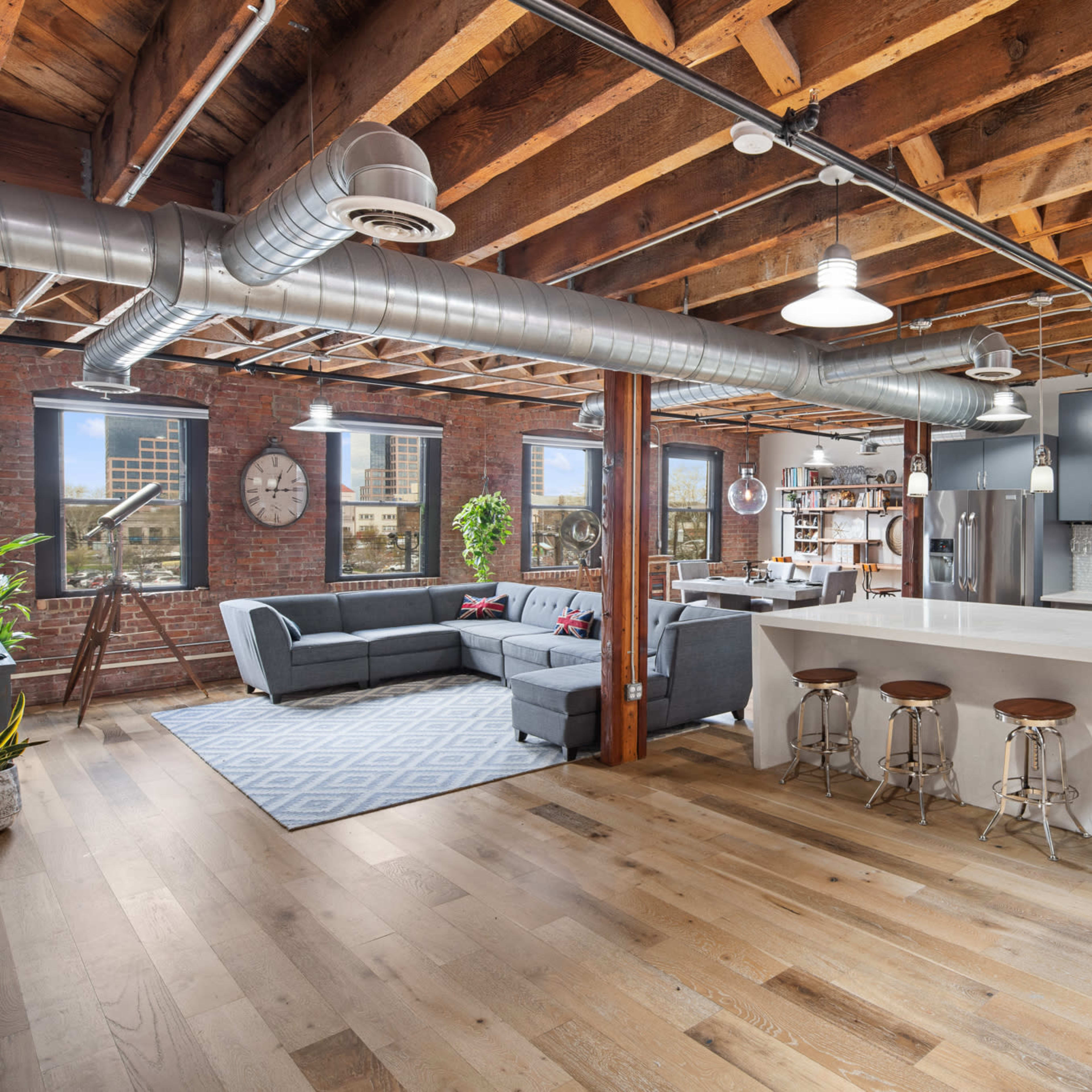 A modern open-concept kitchen and living area with exposed wooden beams, a large island with barstools, and a sectional sofa.