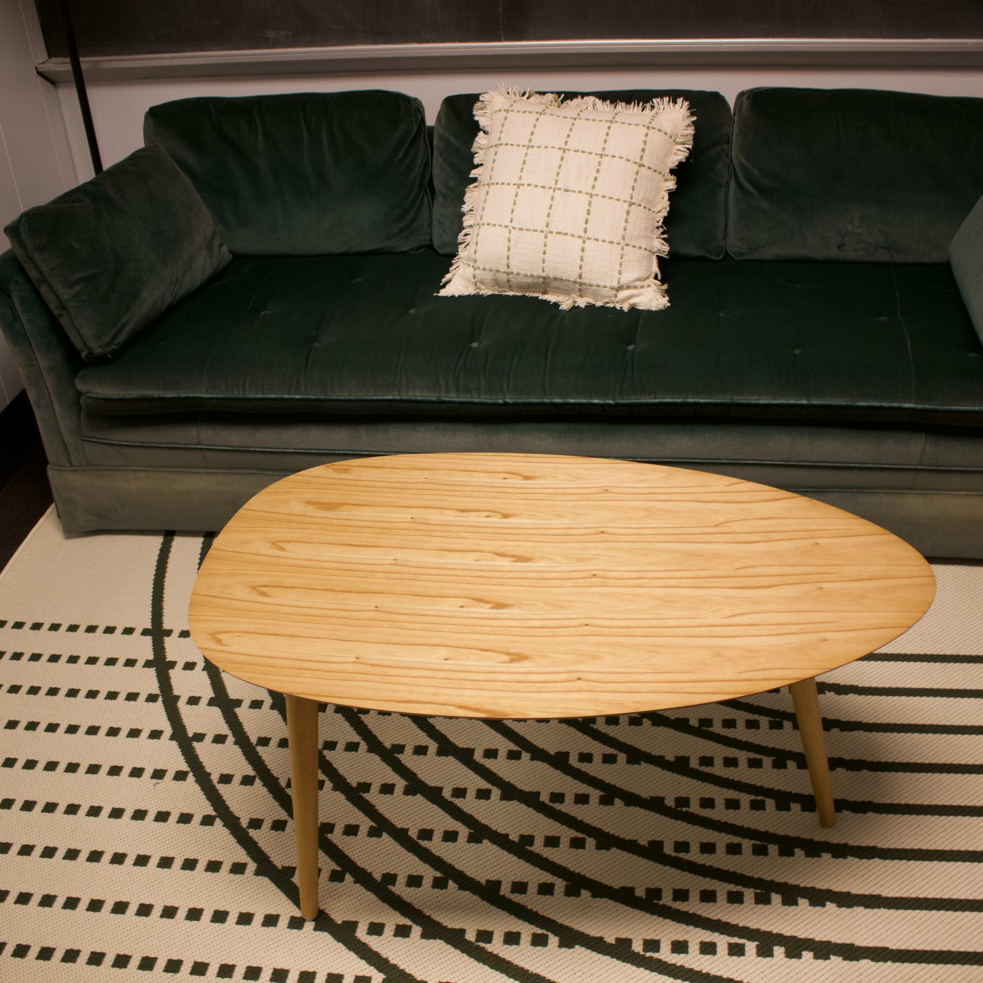 A green couch with a decorative pillow and a wooden, oval coffee table placed on a patterned rug.